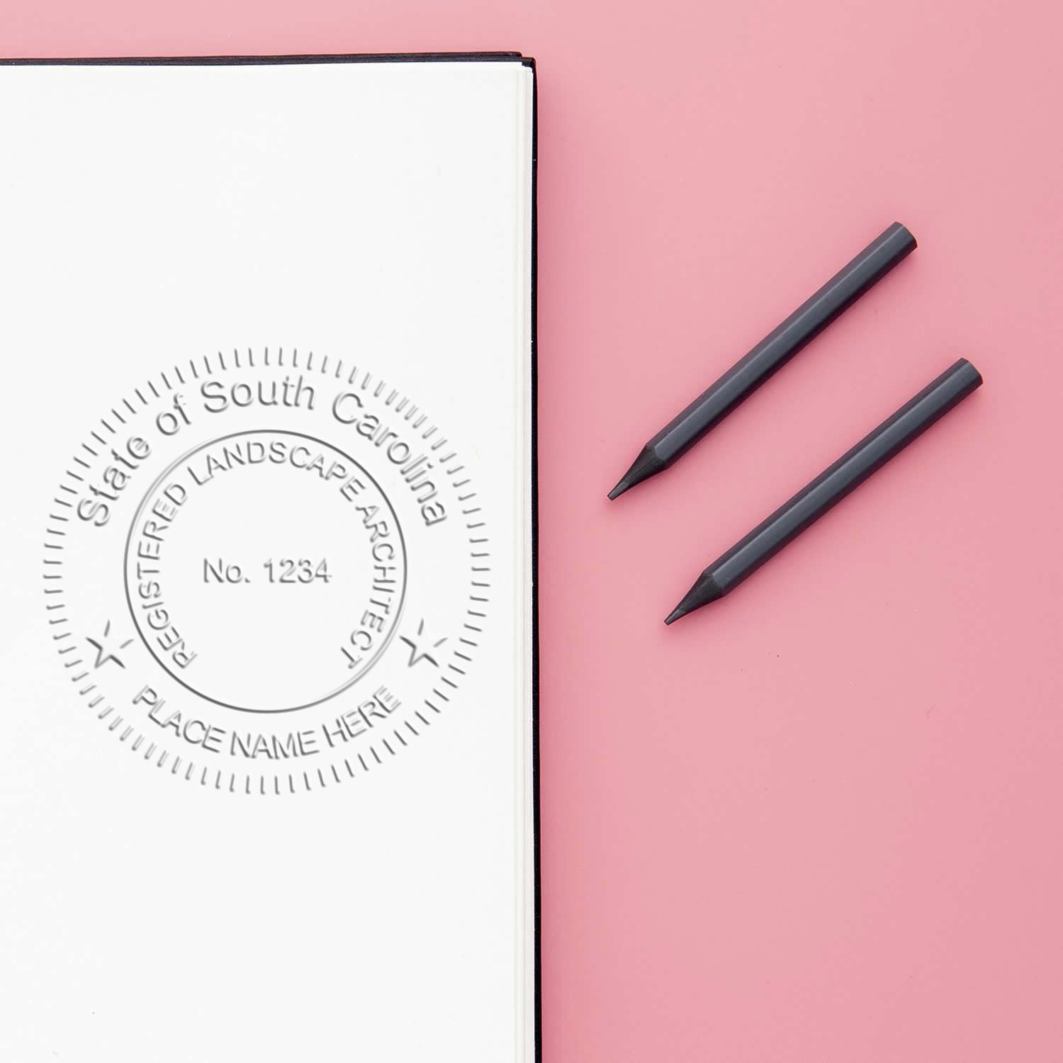 Blank notebook mockup with embossed South Carolina landscape architect seal and two black pencils on a pink background.