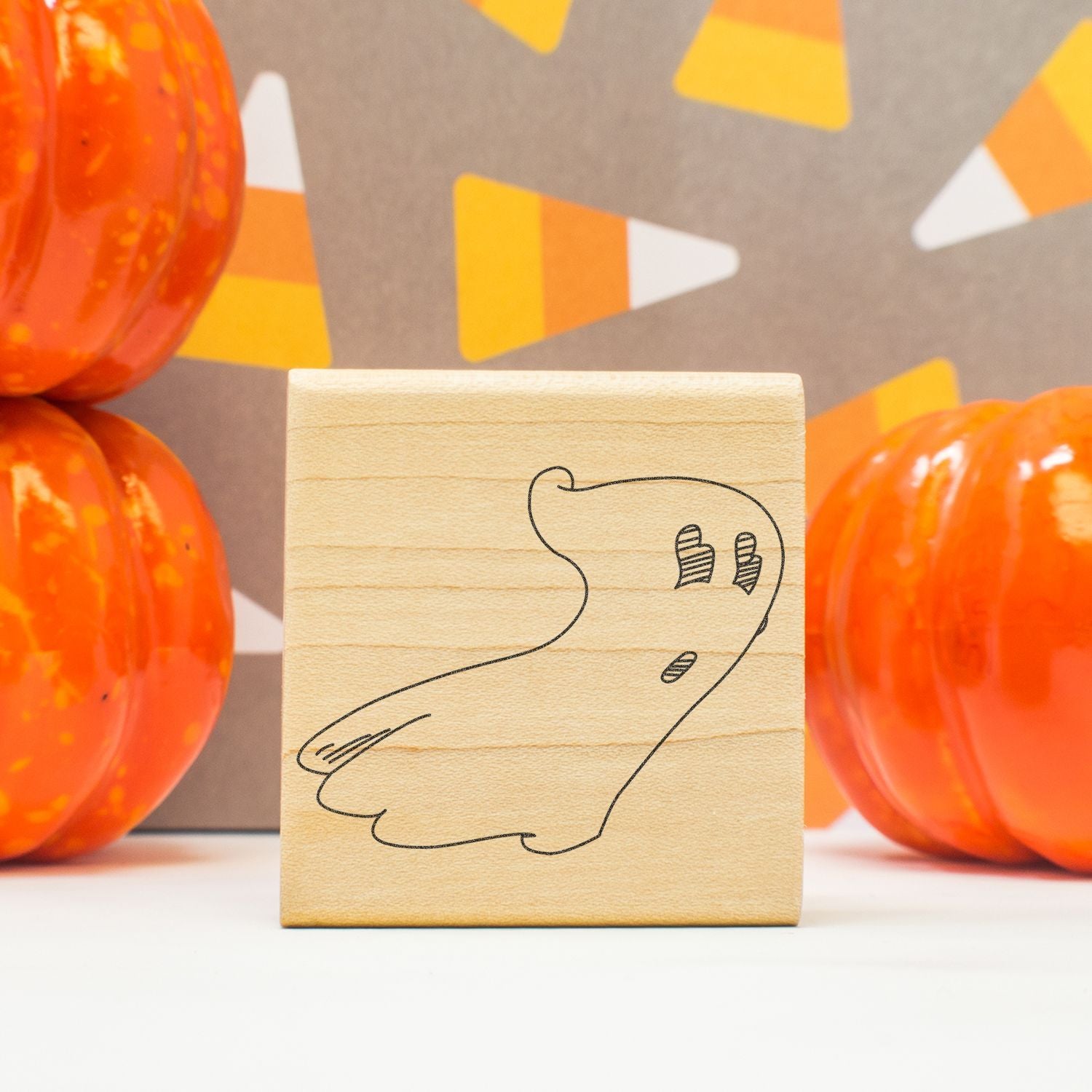 Wooden ghost stamp with Halloween pumpkins and orange festive decor on a craft table.