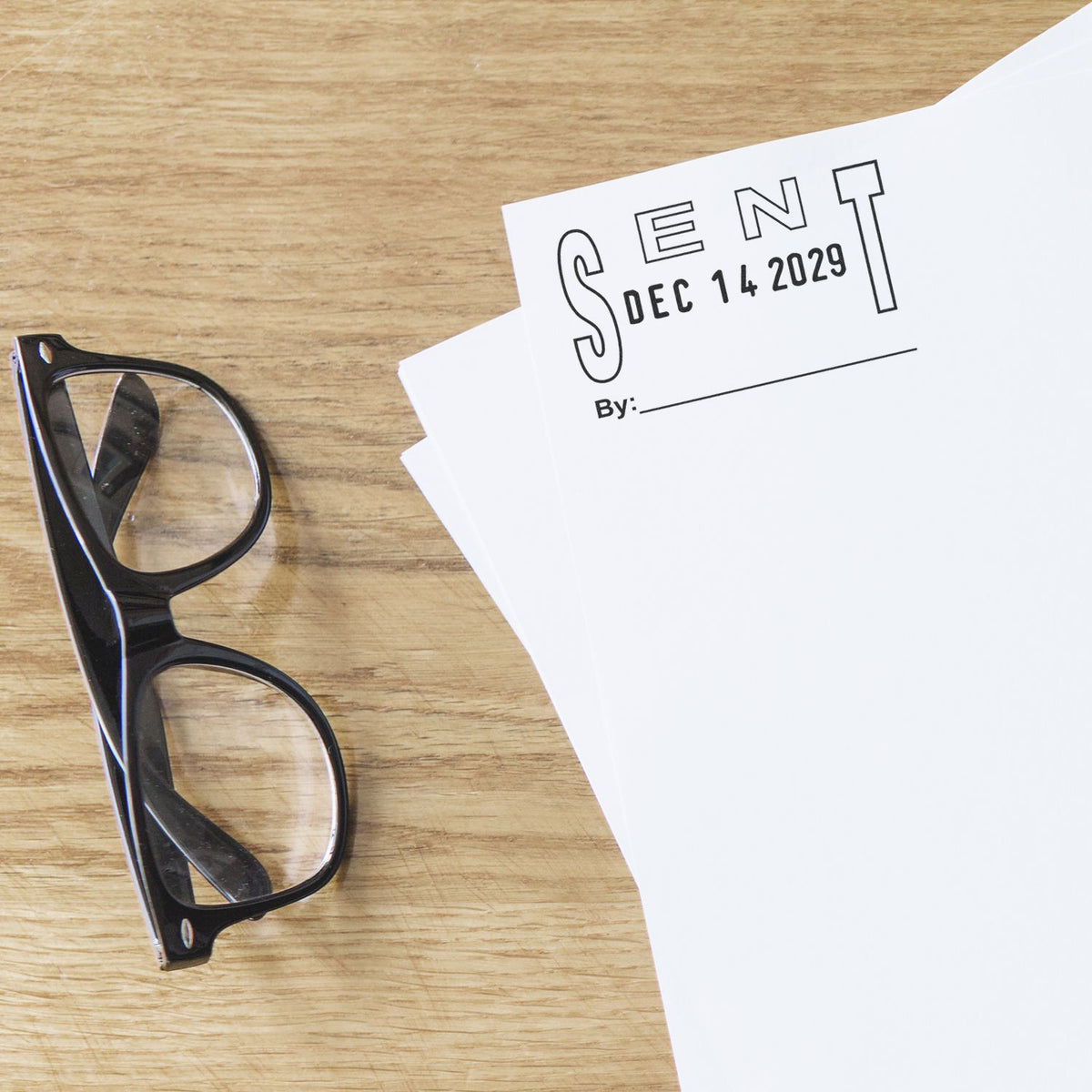 Black eyeglasses beside stamped Sent documents on a wooden desk, business paperwork concept