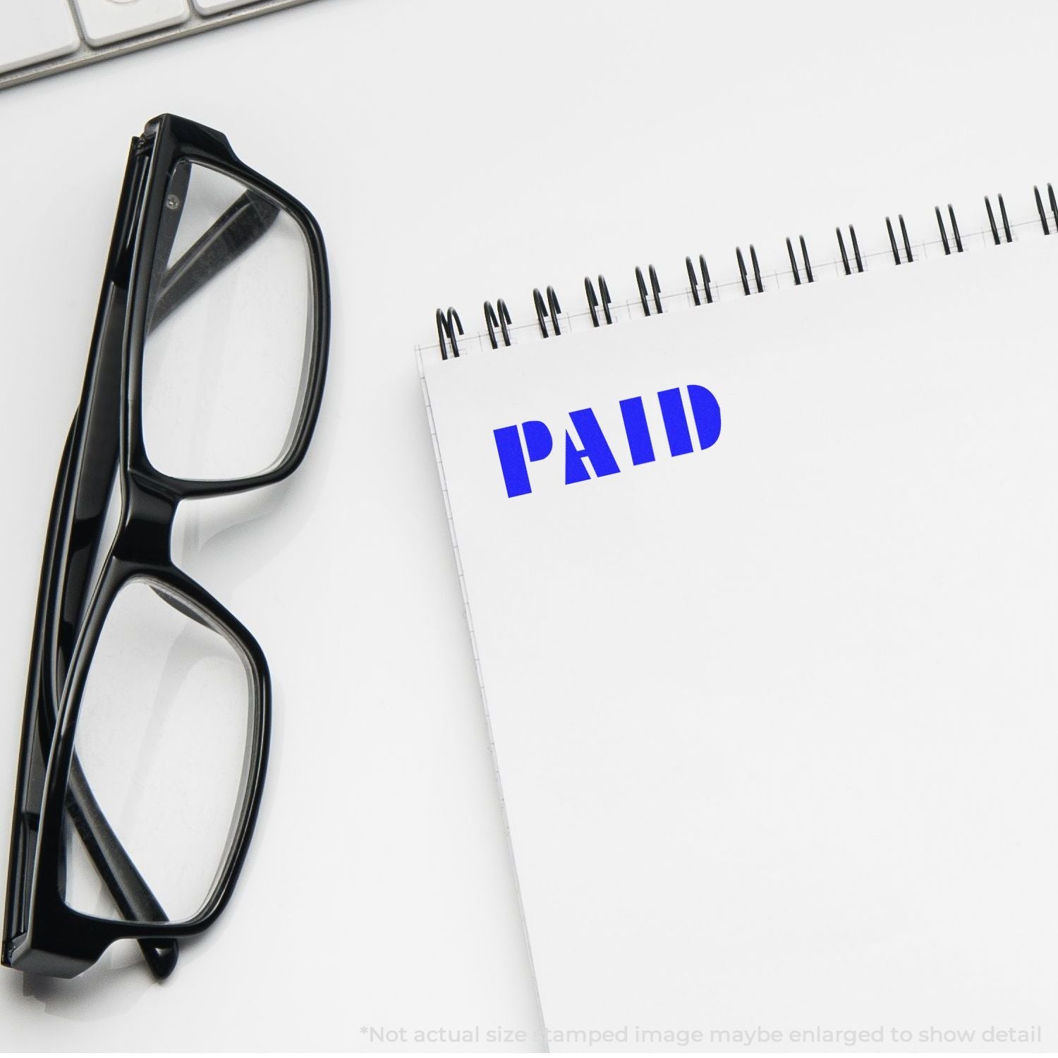 Black eyeglasses beside a spiral notebook stamped PAID on a clean white desk, office finance concept.