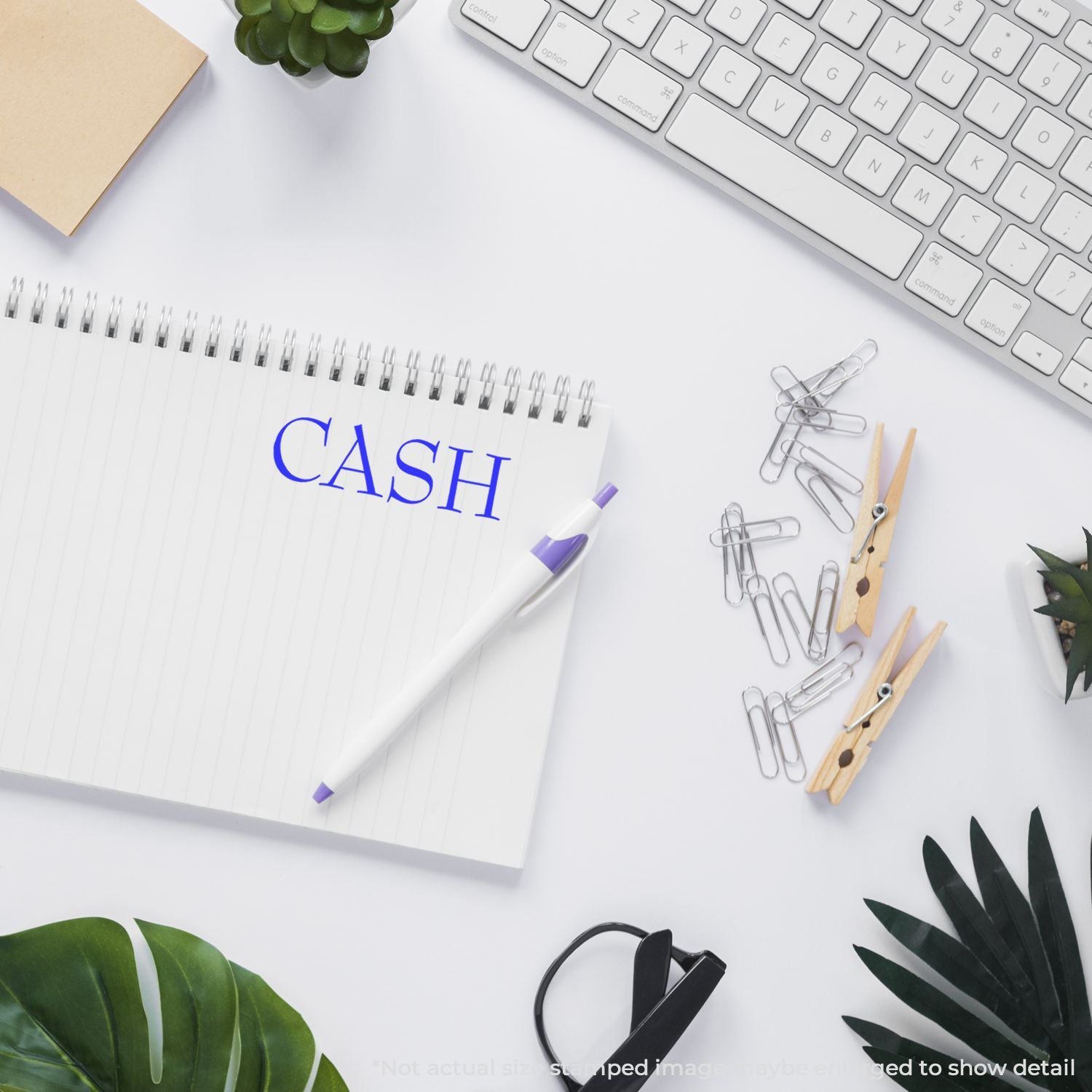Minimal office desk with notebook labeled cash, keyboard, pen, paper clips, and green plants on a white background.