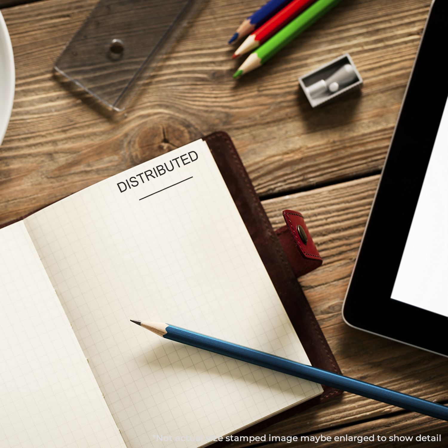 Open notebook labeled DISTRIBUTED on a wooden desk with pencils, tablet, and office supplies.