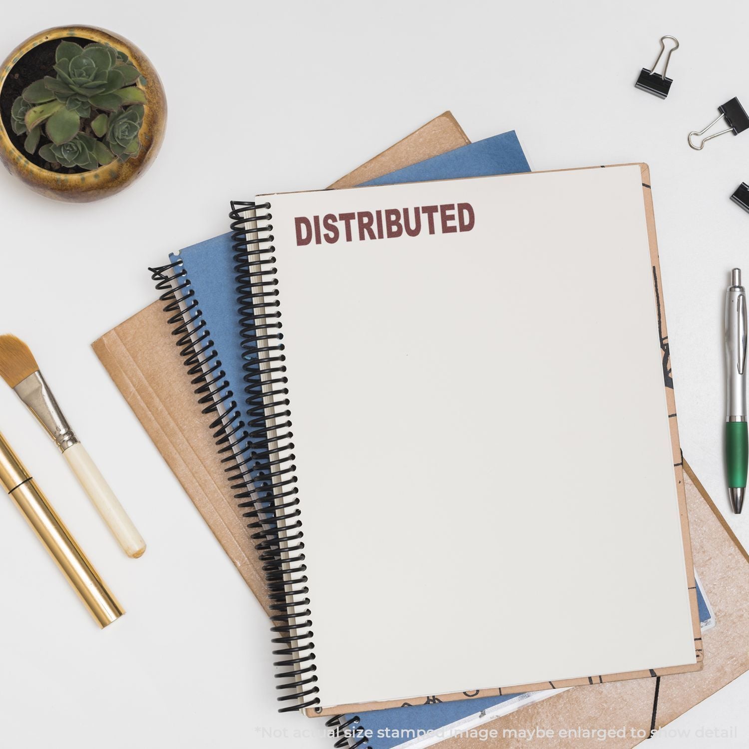 Overhead flat lay of a distributed spiral notebook with stationery, pens, notebooks, and a small succulent plant on a white desk.