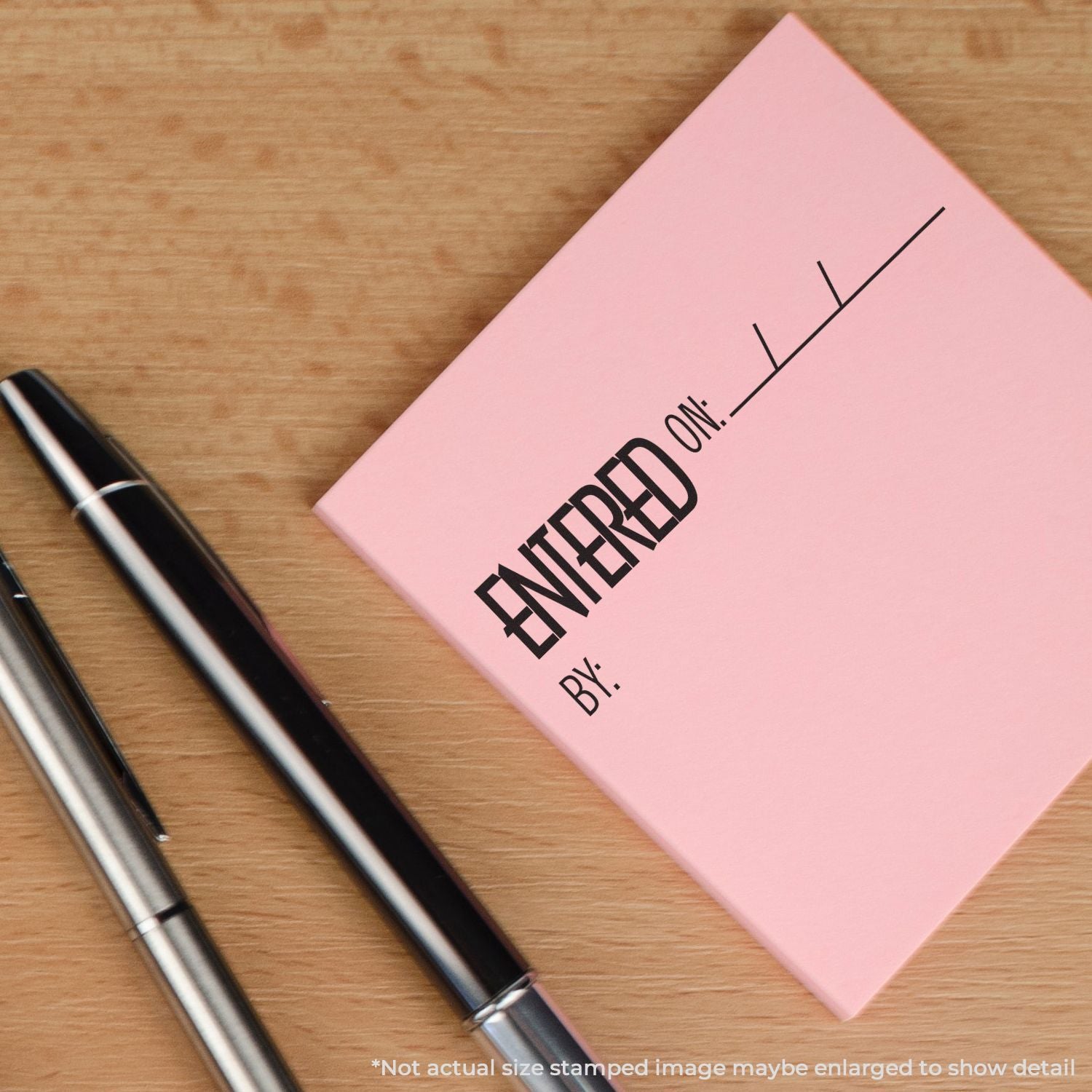 Pink notebook with stamped Entered text and a pen on a wooden deskwriting, journaling and office stationery for notes and planning.