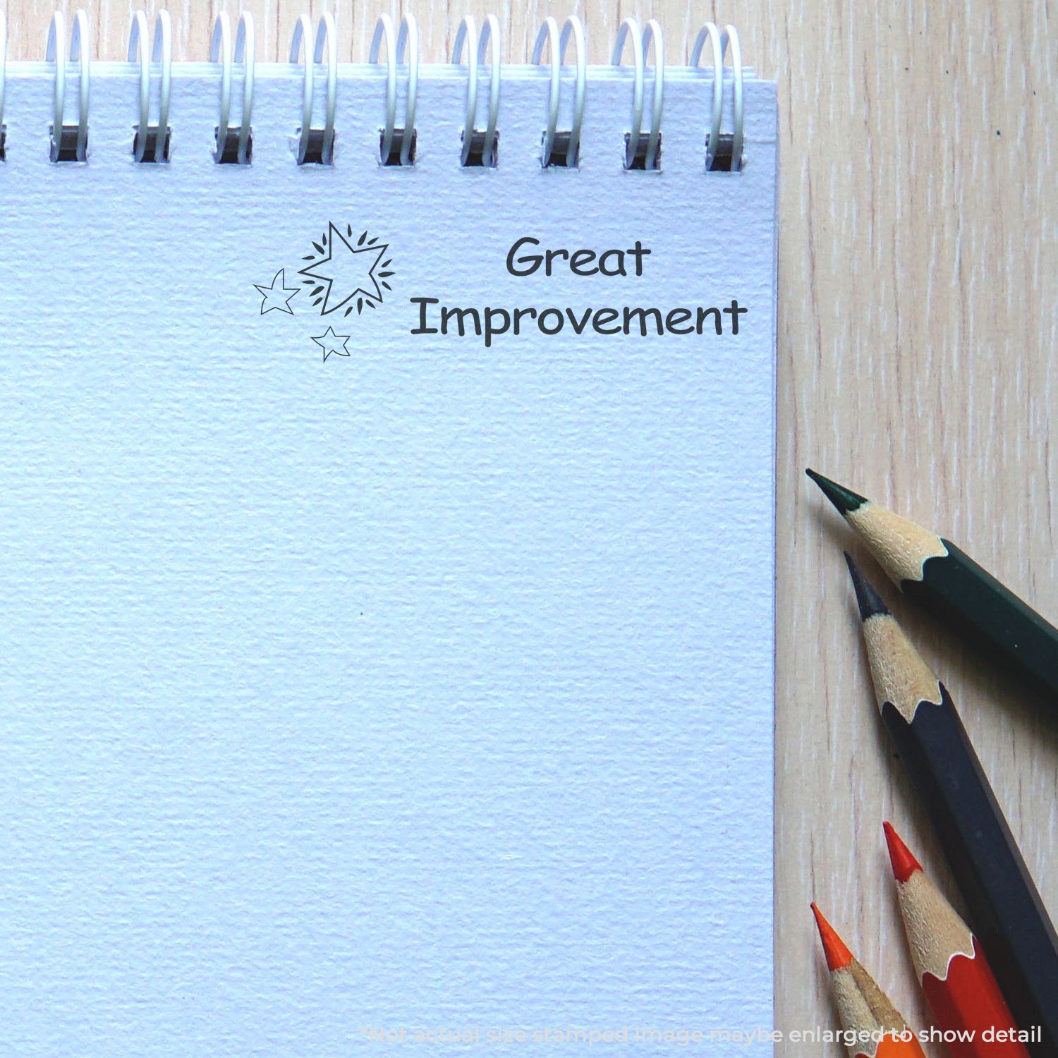 Spiral notebook with Great Improvement text and colored pencils on a wooden desk.
