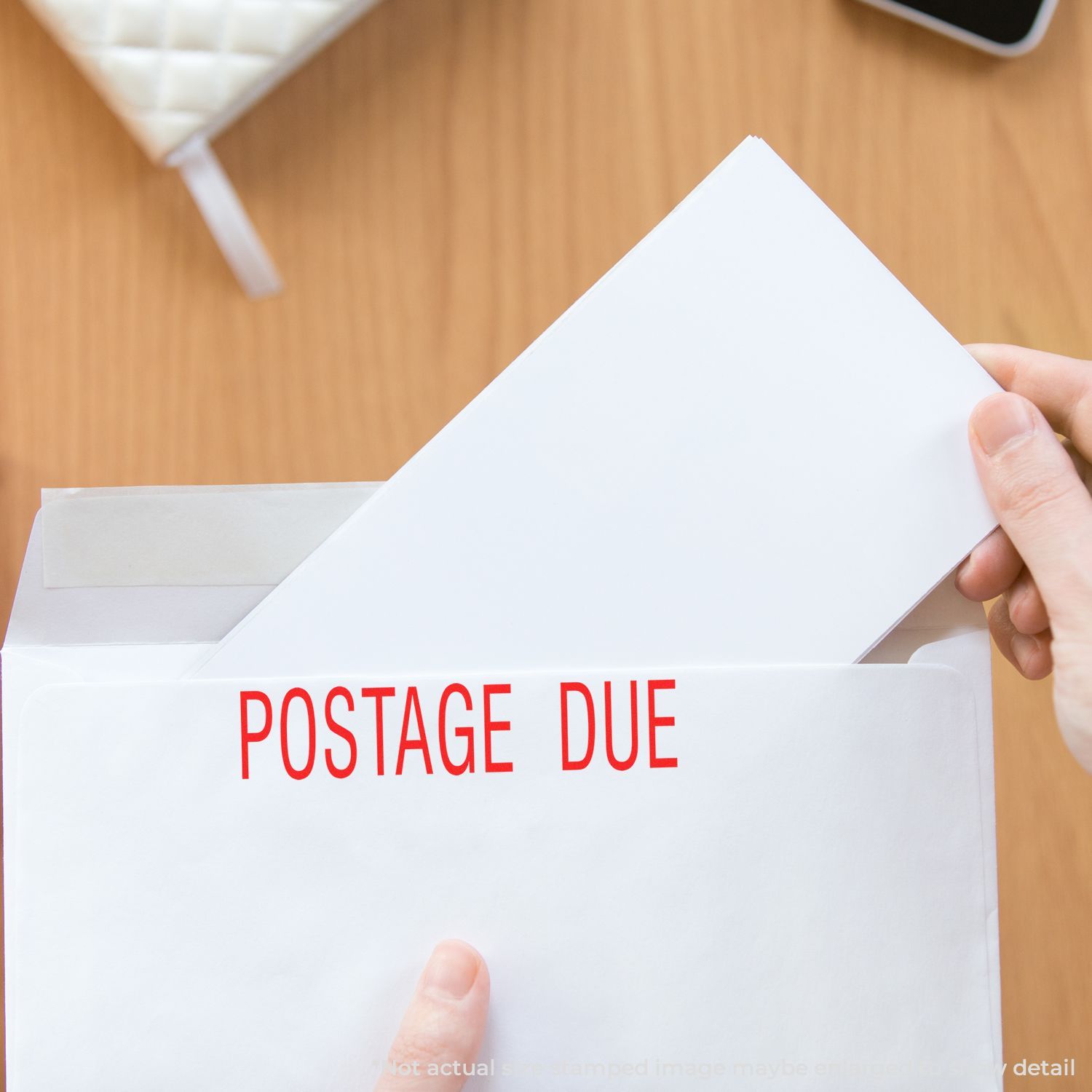 Hand opening a postage due envelope on a wooden desk, showing returned mail with red postage due text.