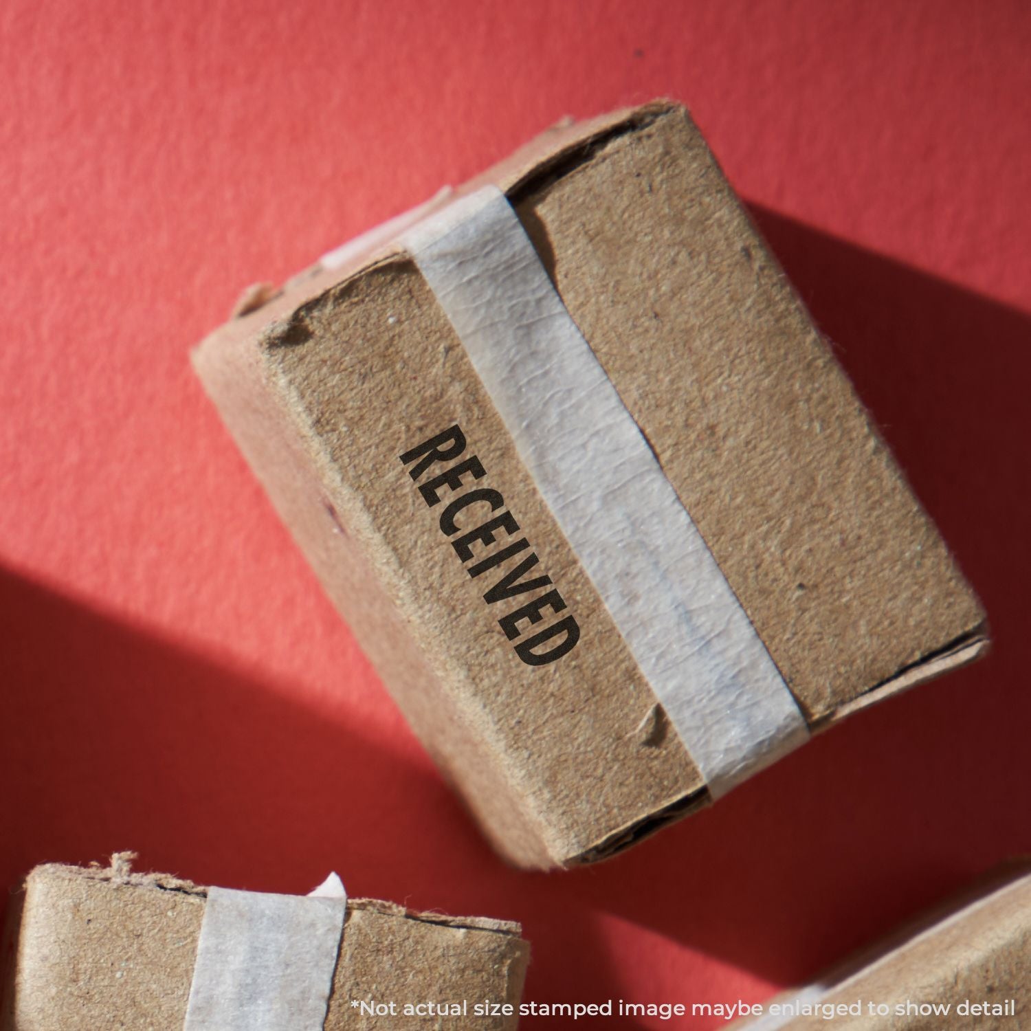 Cardboard shipping package stamped RECEIVED on a red background, close-up parcel delivery box image.