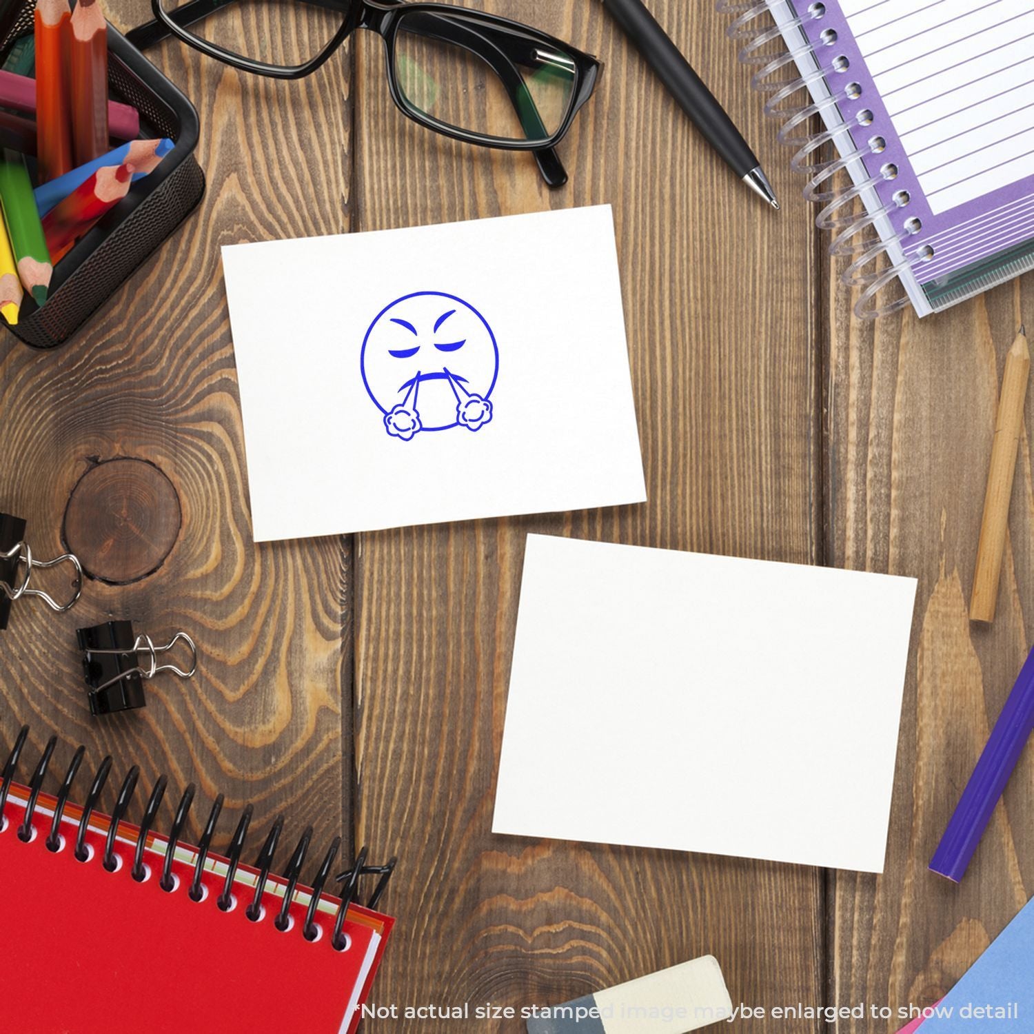 Top view of office and school supplies on a wooden desk, with blank sticky notes, notebook, glasses, colored pencils, and an angry face doodle on paper.