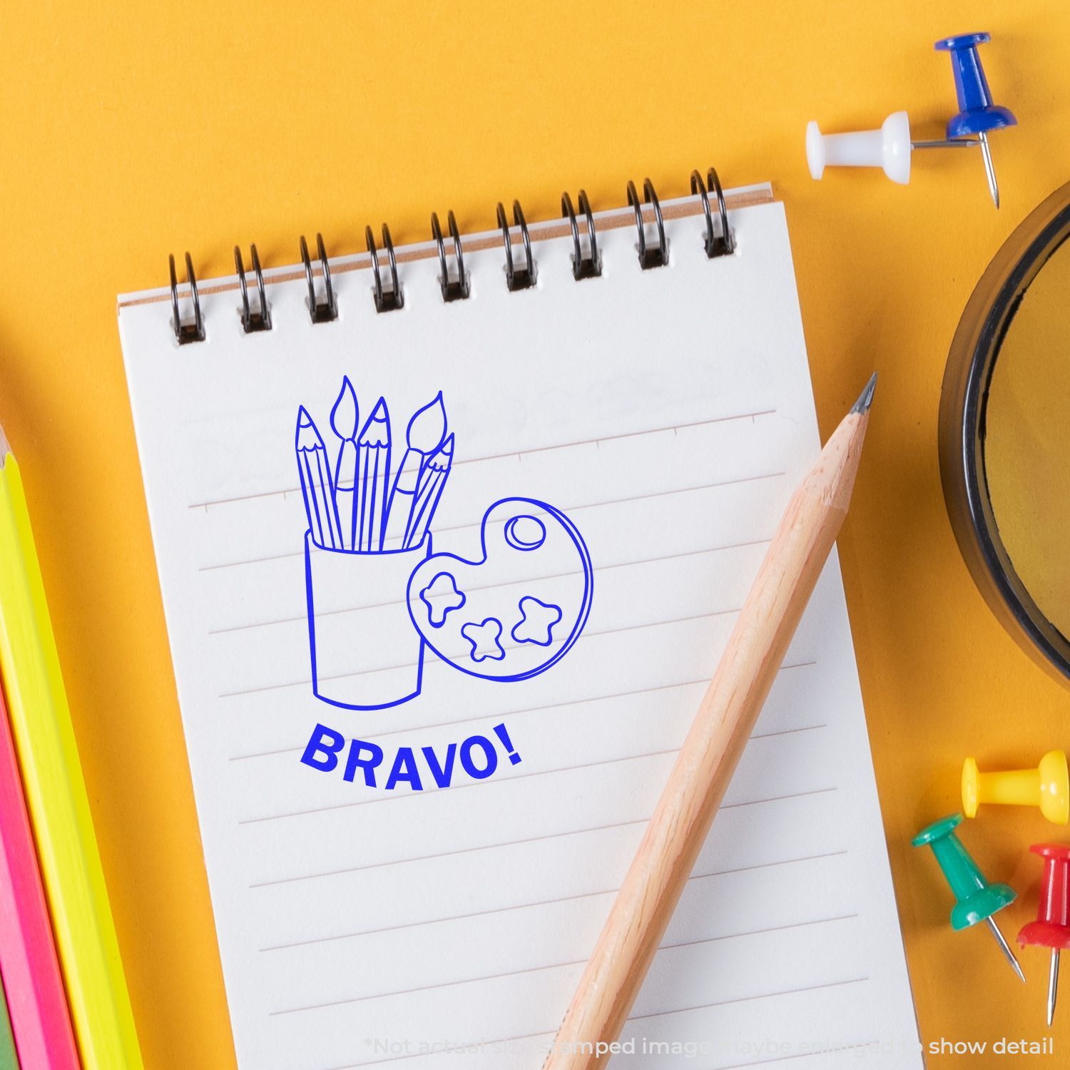 Notebook with Bravo art supplies icon, pencils, and colorful push pins on a yellow background.