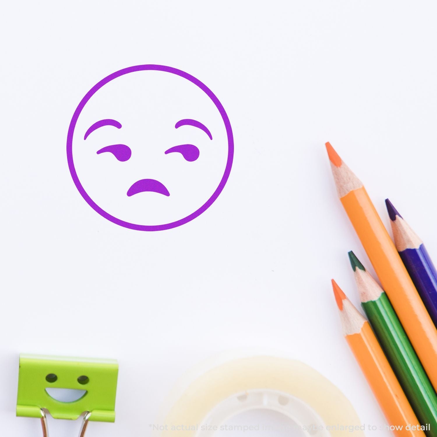 Sad purple emoji face drawing on white paper with colored pencils and a smiling binder clip.