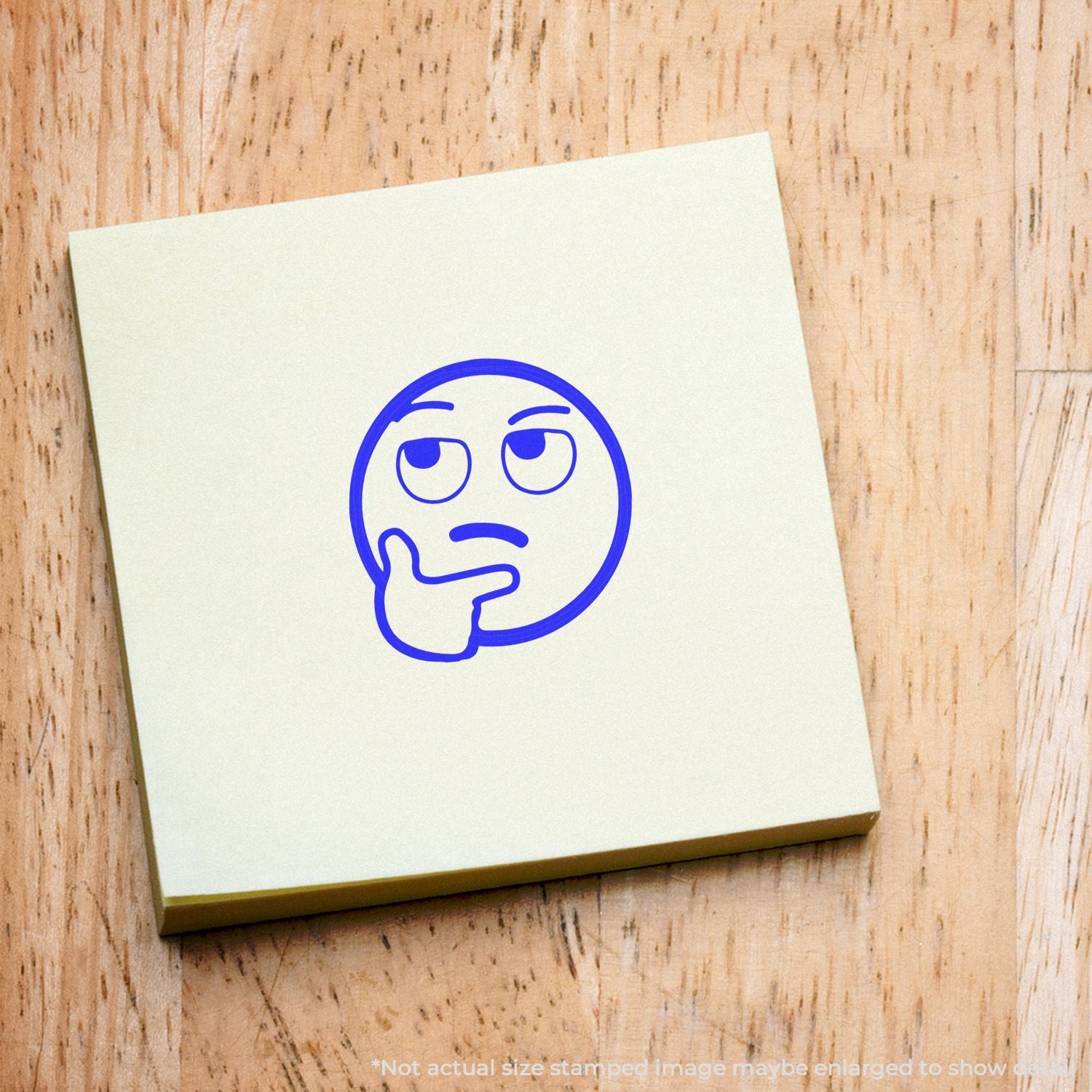 Thinking face emoji stamp on a cream sticky note on a wooden background.