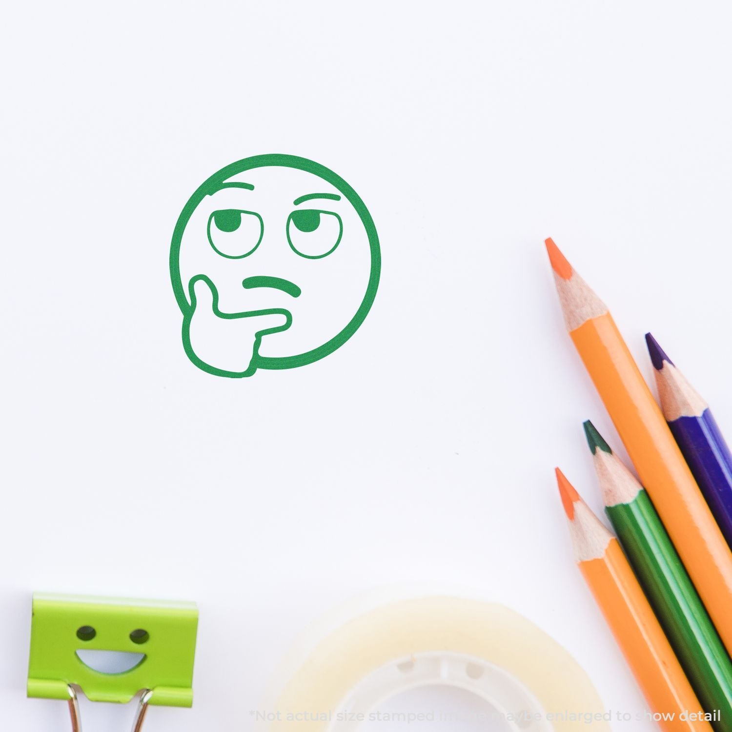 Green thinking emoji stamp on white paper with colorful pencils and school supplies, creative stationery concept.