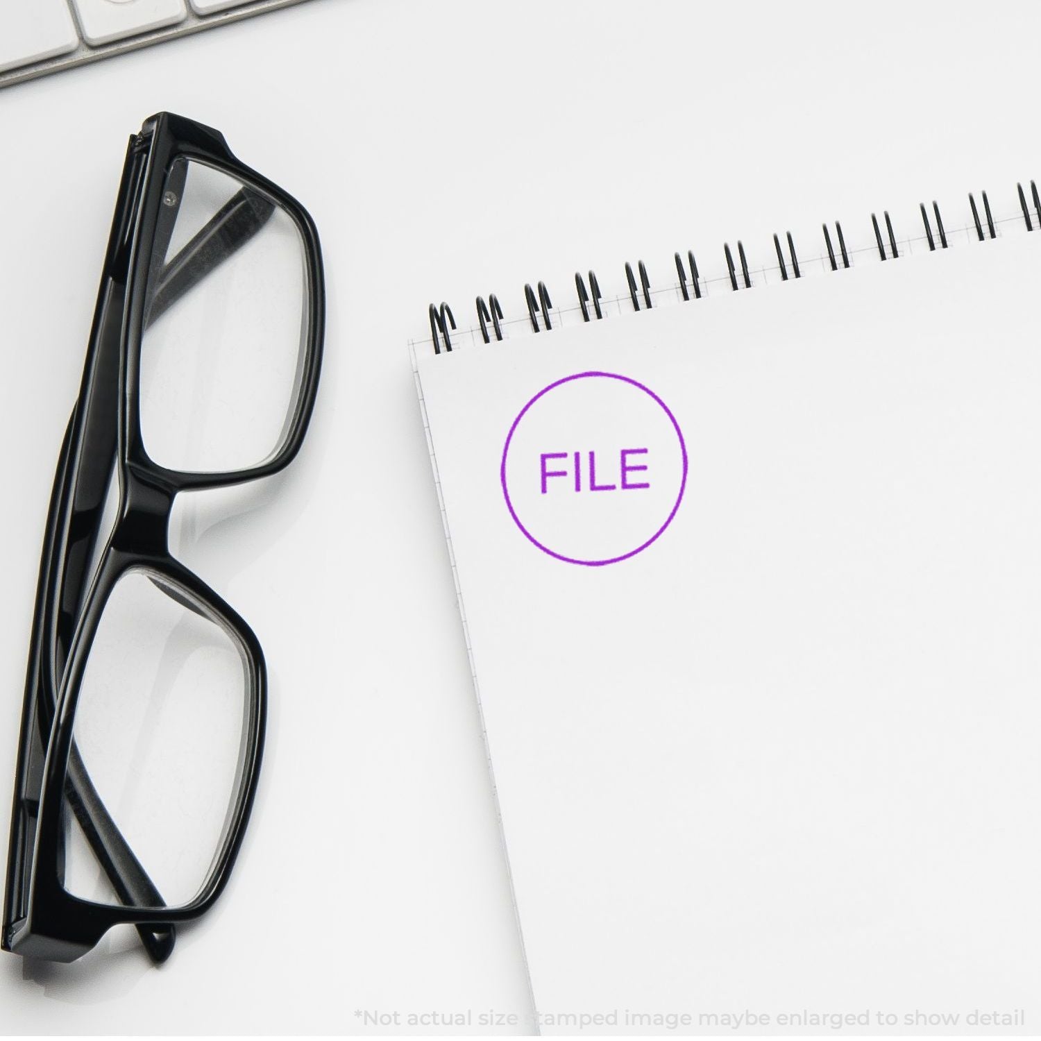 Black eyeglasses beside a white spiral notebook with a purple FILE stamp on a clean office desk background.