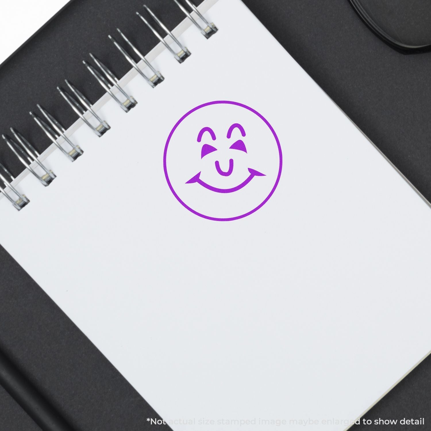 White spiral notebook with purple smiley face icon on a black desk, minimal office stationery design