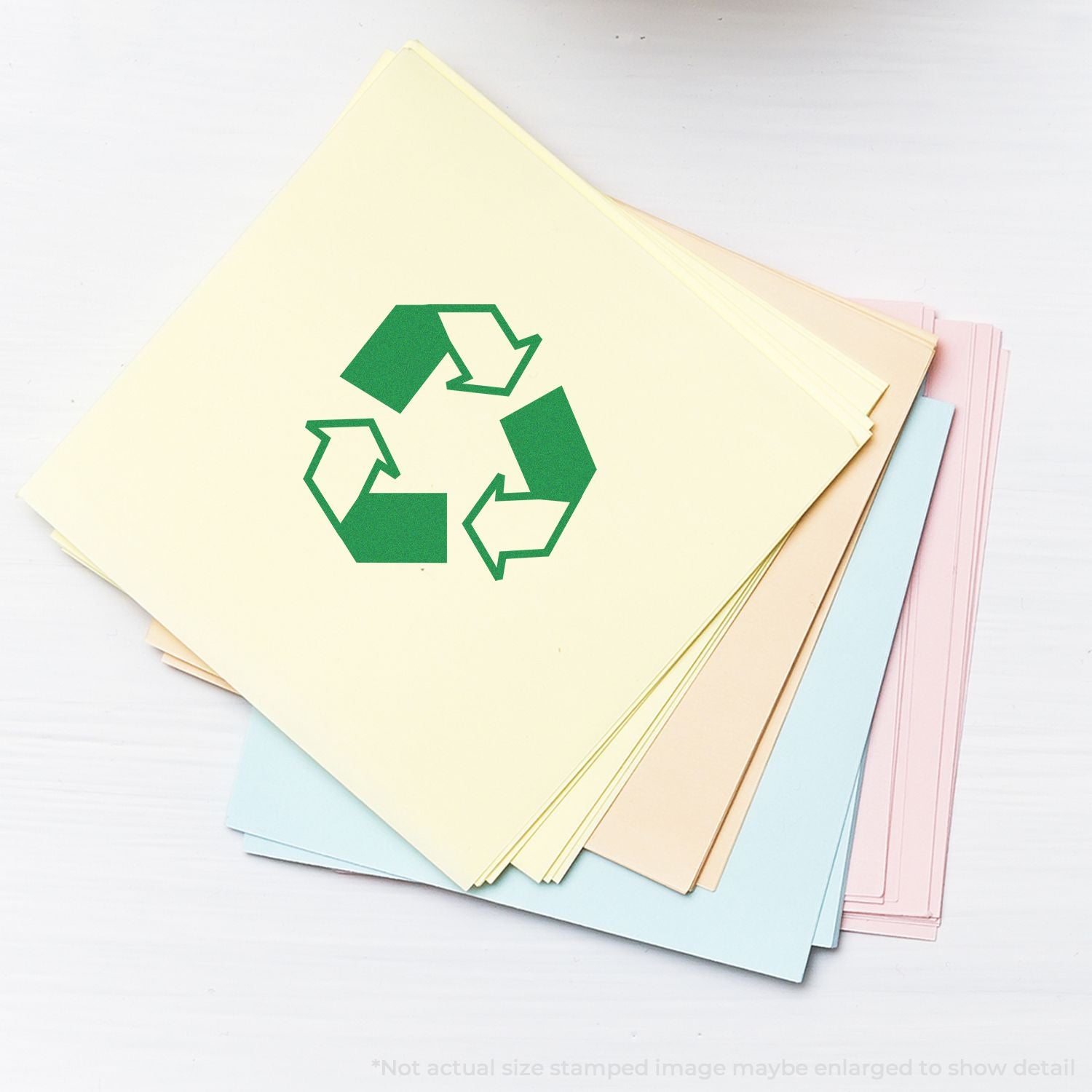 Stack of colorful recycled paper sheets with green recycle symbol on top