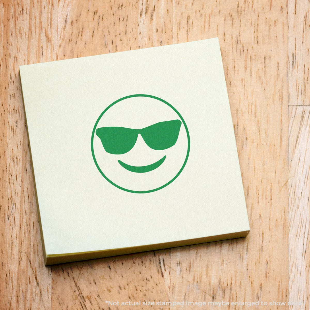 Green cool smiley emoji with sunglasses on a white note on wood, representing a trendy social media reaction for emoji marketing.