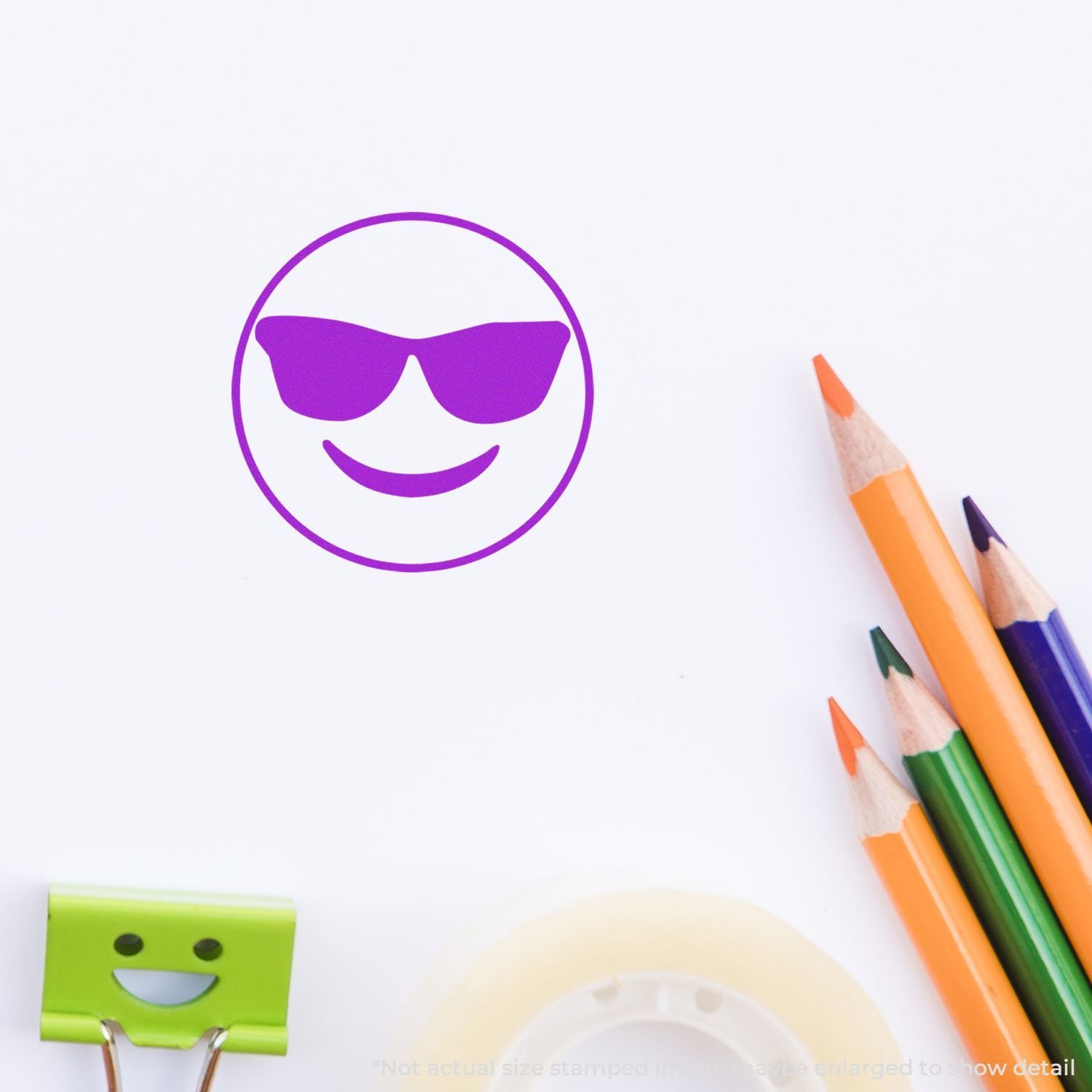 Purple sunglasses smiley face stamp on white paper with colorful pencils and office supplies.