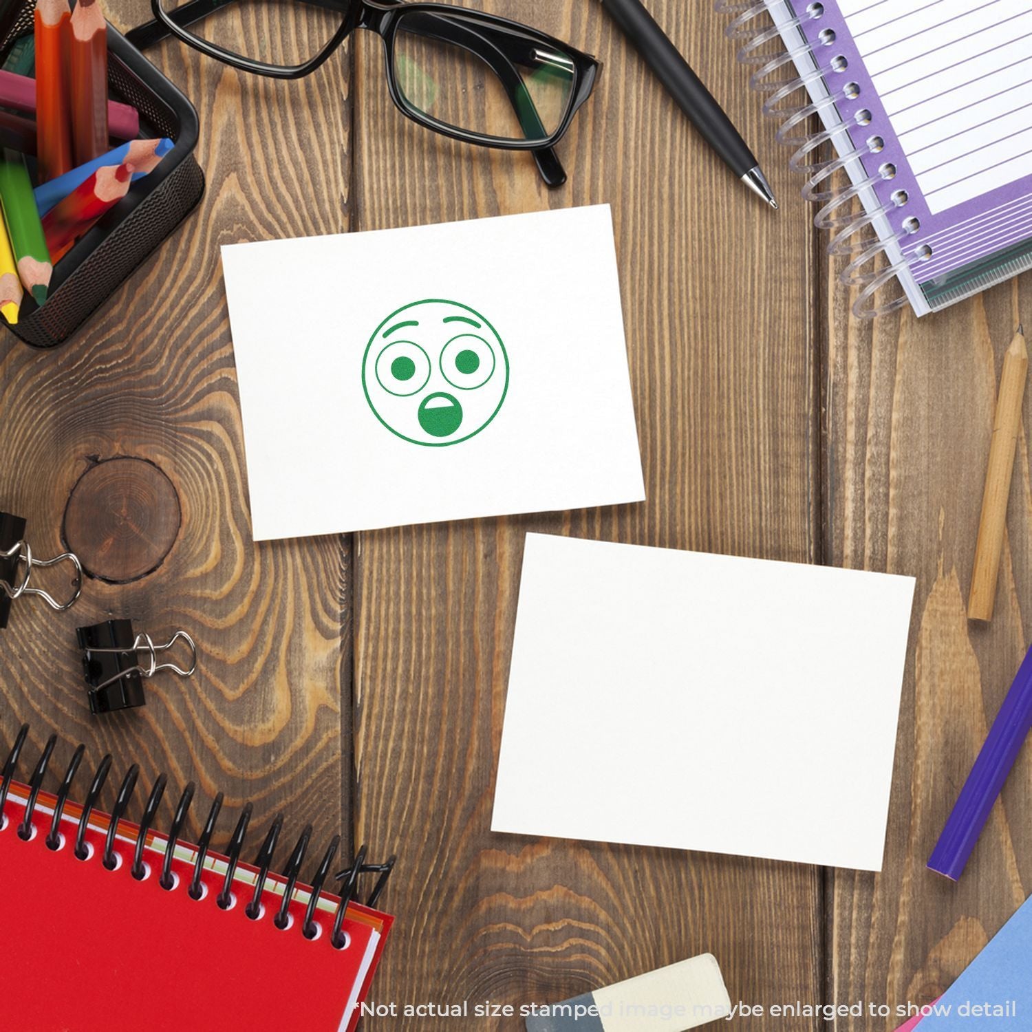 Top view of office desk with stationery, notebooks, glasses, pens, and a sticky note showing a surprised emoji icon on a wooden table.
