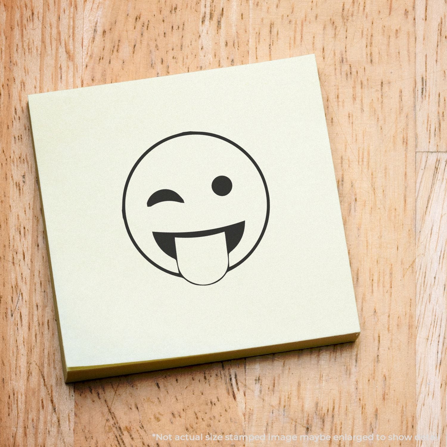 Winking tongue-out emoji on a sticky note over a wooden background, fun playful icon design.