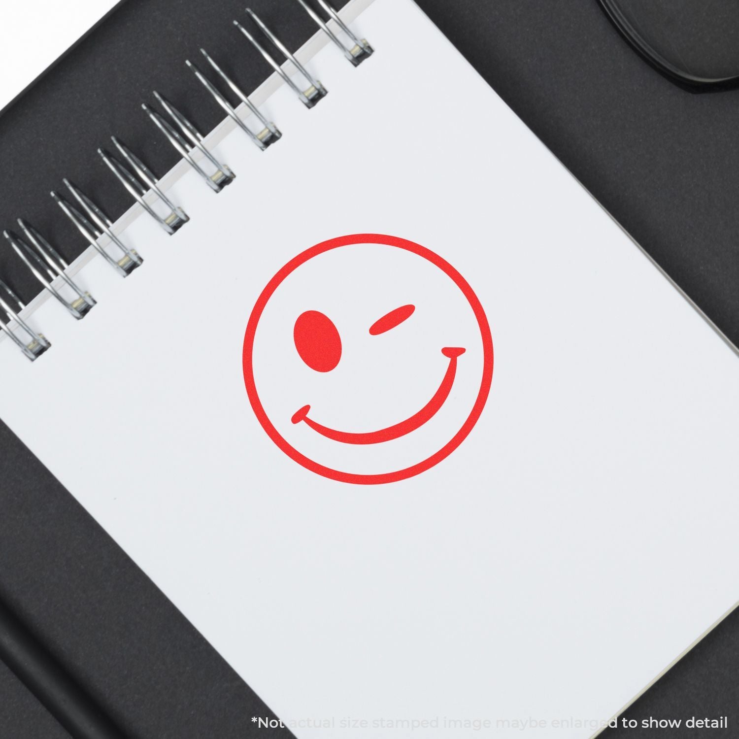 Red winking smiley face on a blank spiral notebook page on a black desk background