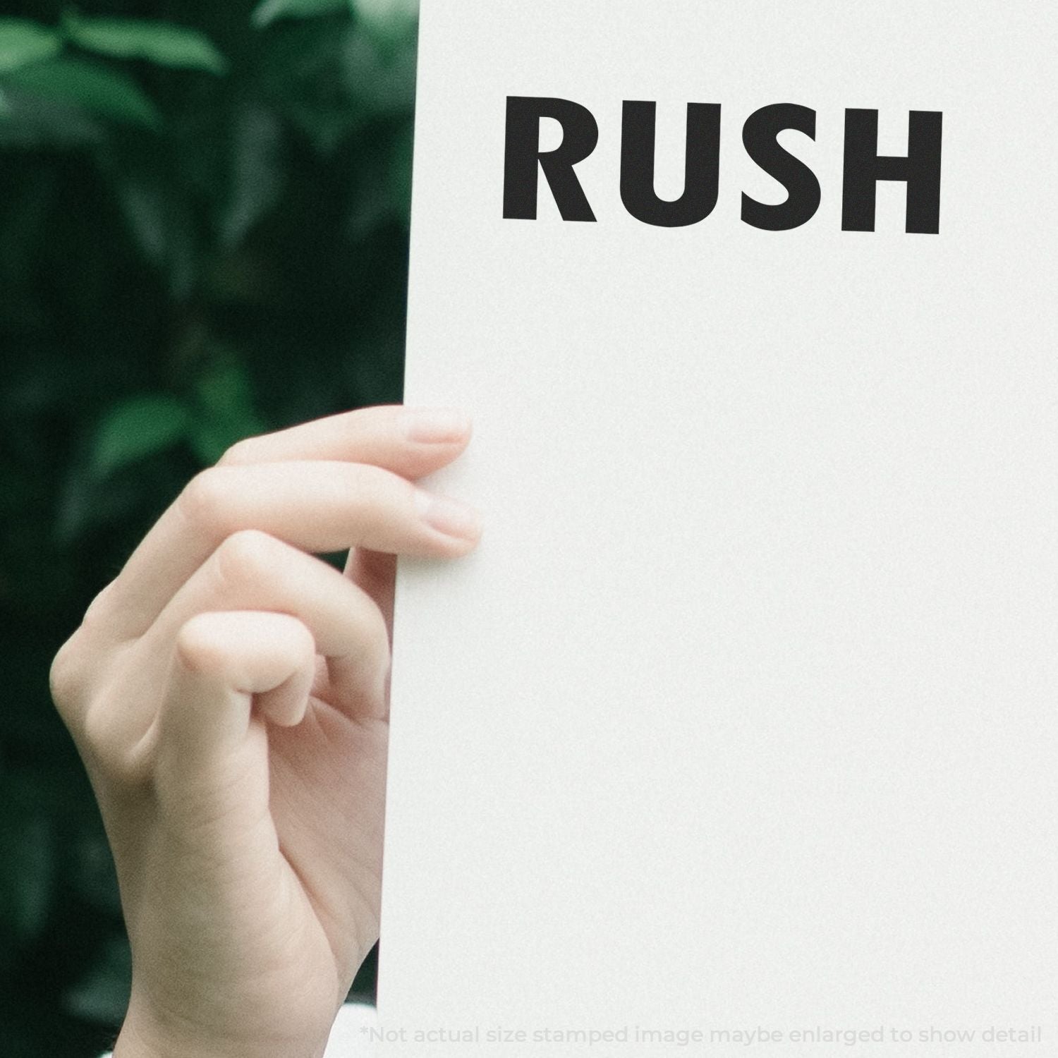 Close-up of hand holding a white sign with bold RUSH text against a blurred green background.