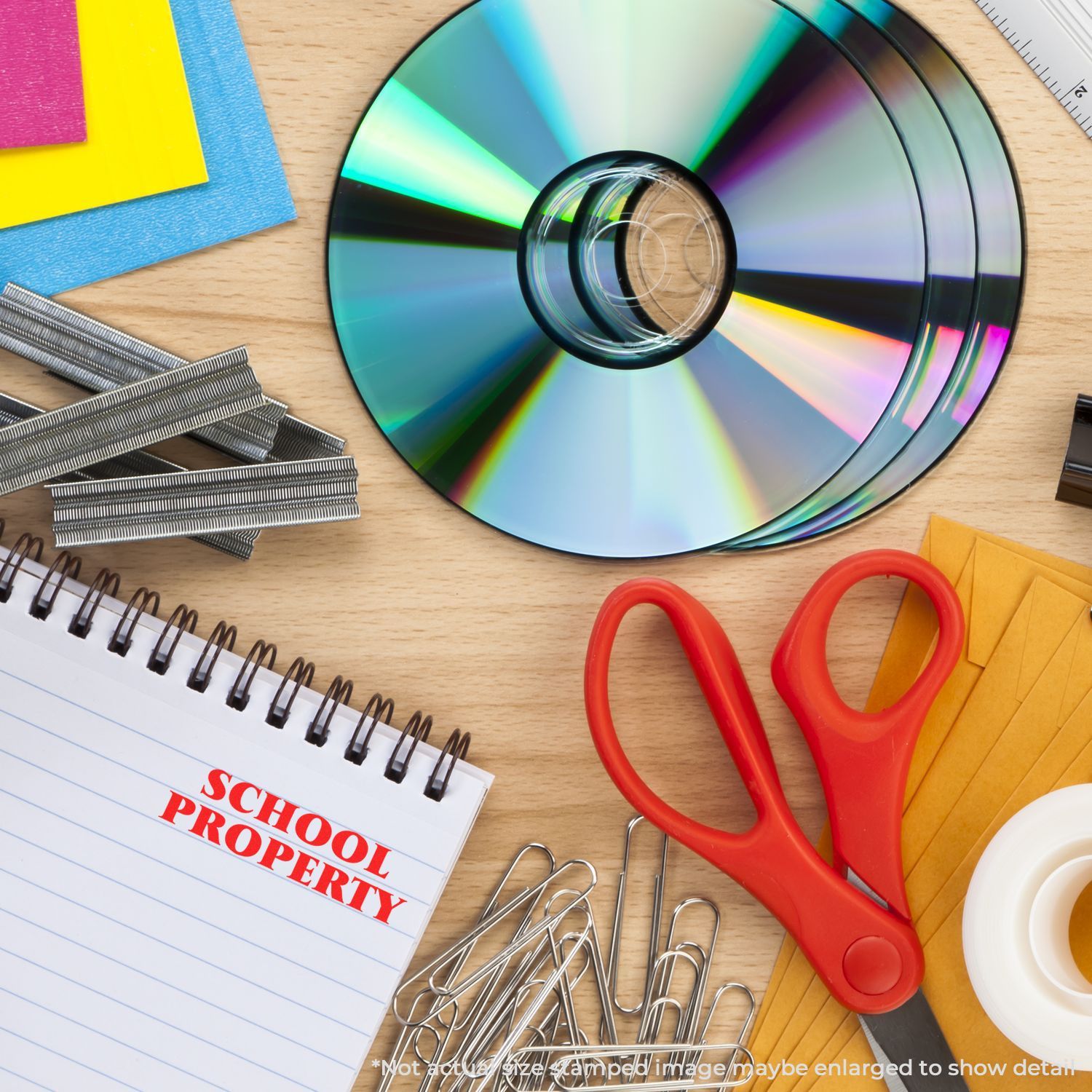 School supplies and stationery on a desk, including scissors, notebook, paper clips, sticky notes, and CDs.