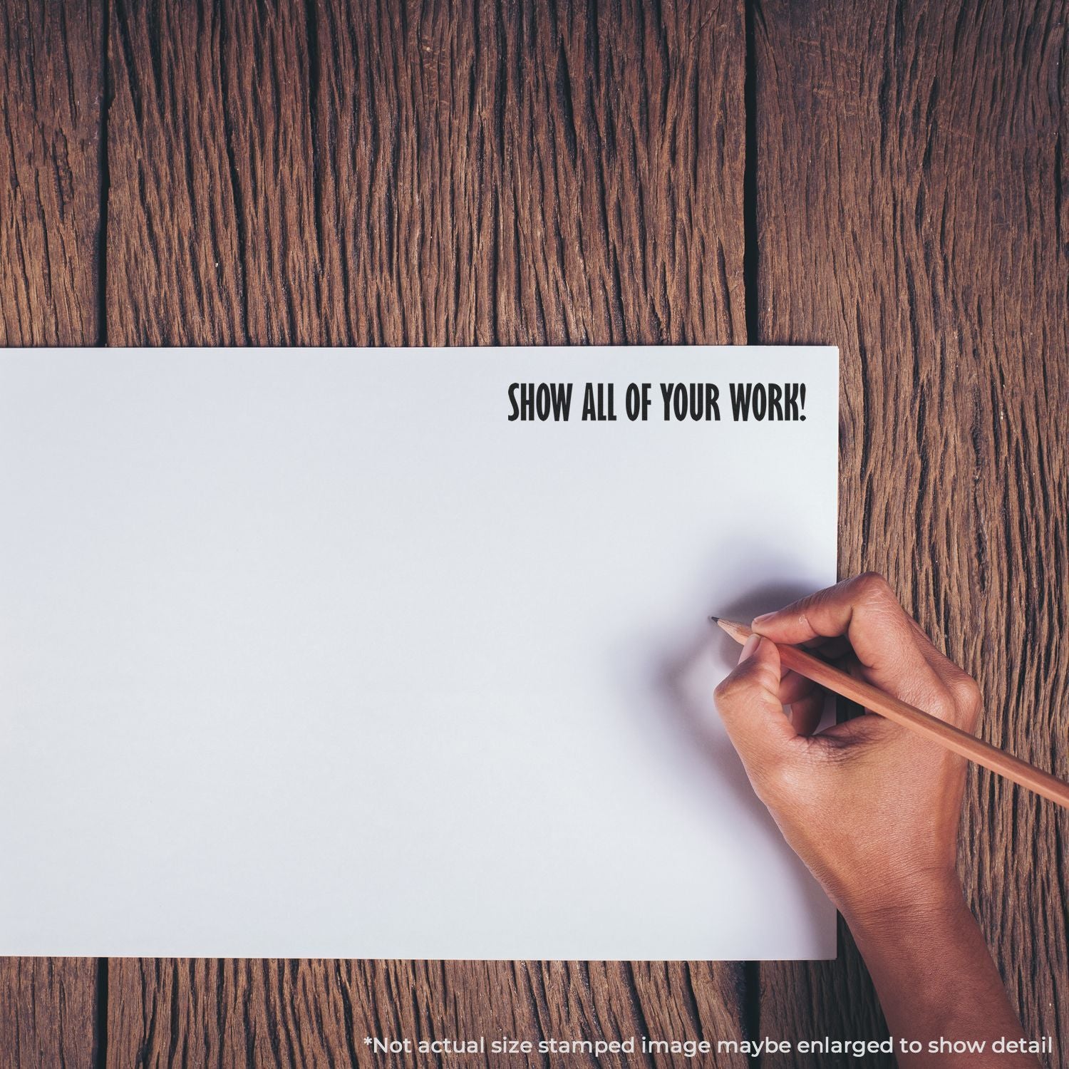 Hand holding pencil over blank paper that says Show All of Your Work on wooden deskencourages homework steps and math process.