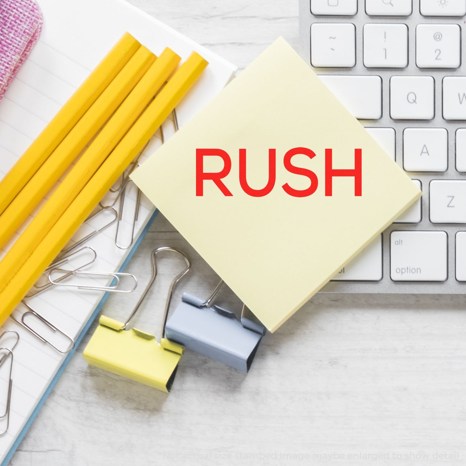 Rush reminder note on office desk with keyboard, pencils, paper clips, and notebooks for urgent business task planning