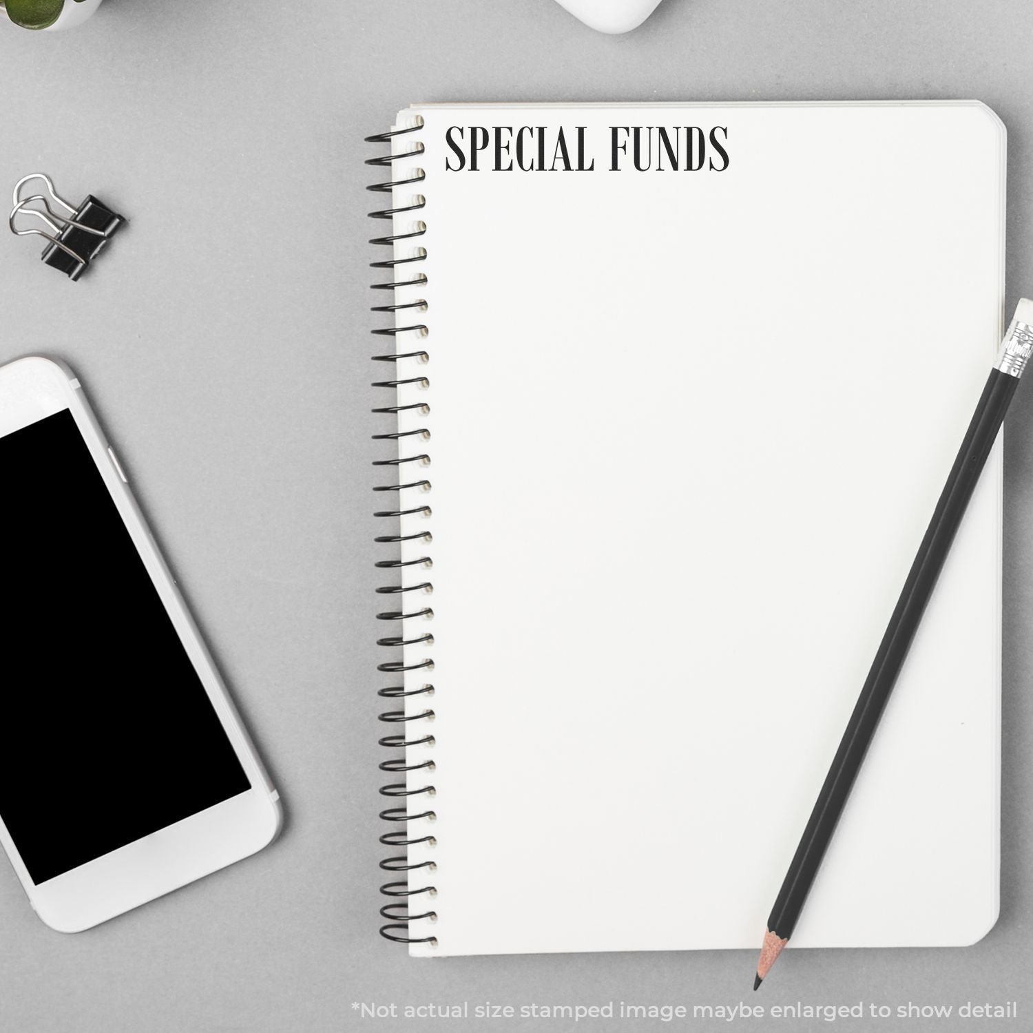 Blank spiral notebook labeled Special Funds with pencil, smartphone, and binder clip on a gray desk.