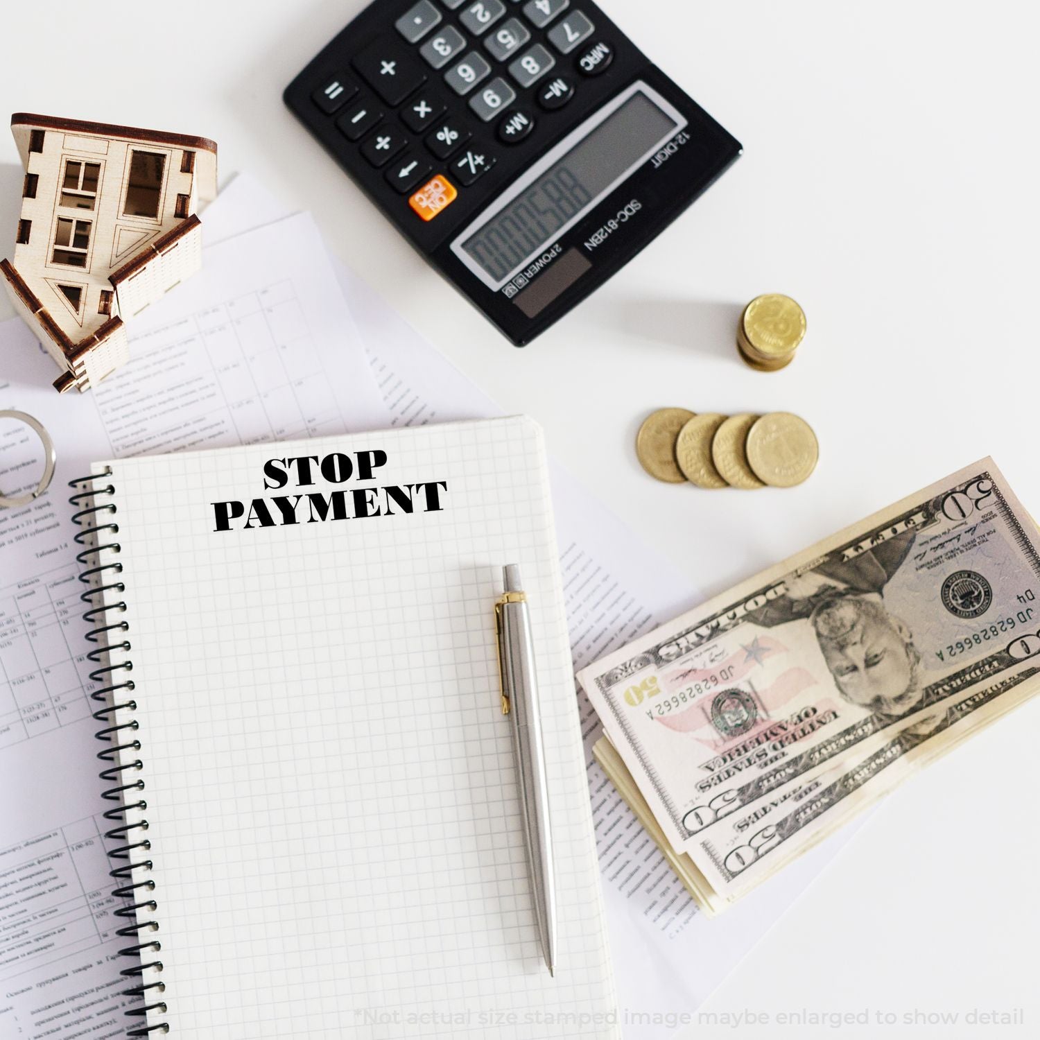 Stop payment concept with notebook, calculator, house model, cash, coins, and financial documents on a white desk.
