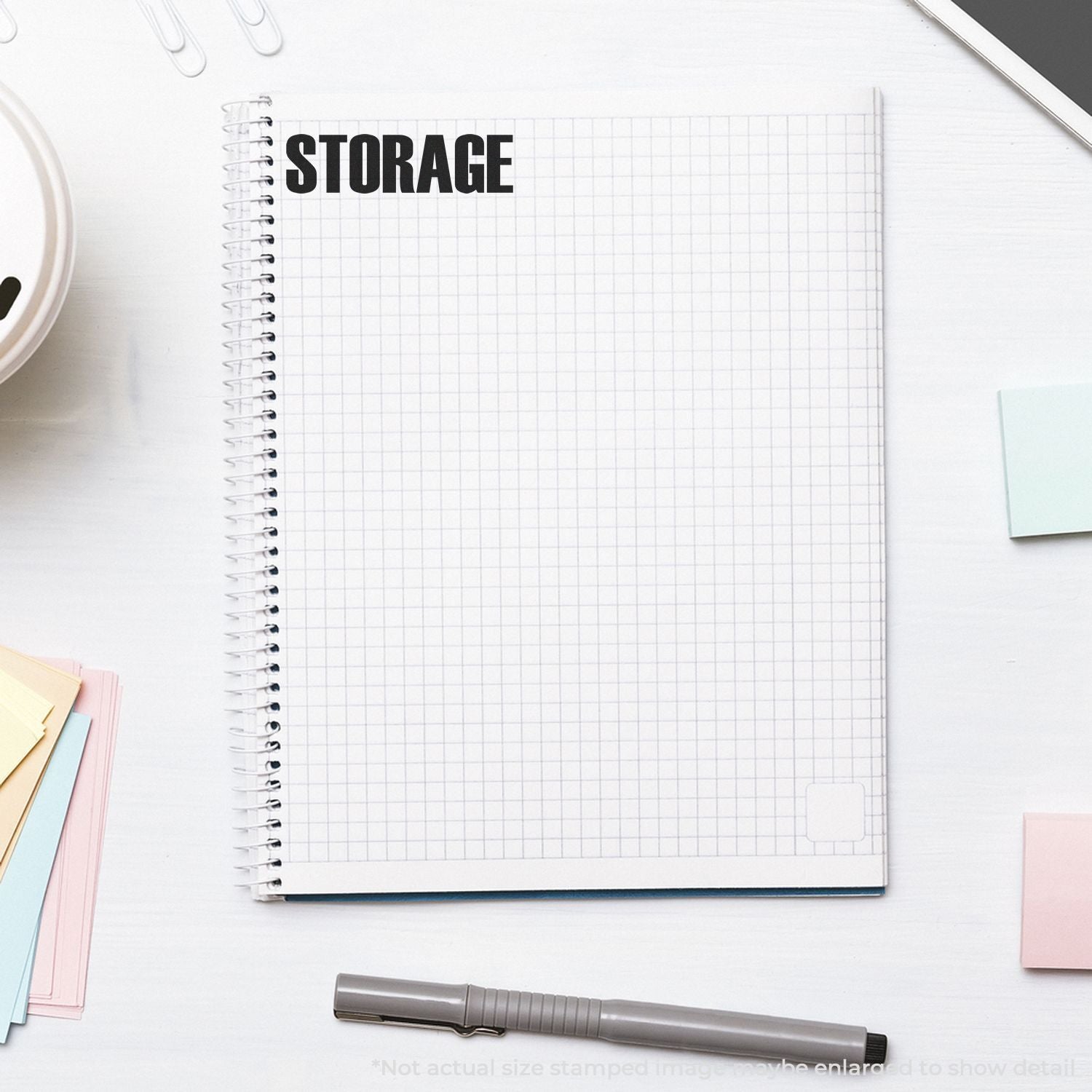 Minimalist spiral notebook labeled STORAGE on a white desk with stationery, paper clips, sticky notes, and pen flat lay.