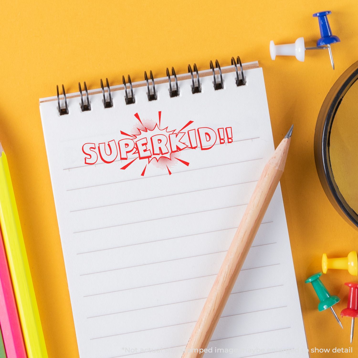 Spiral notebook with SUPERKID!! text, pencil, and colorful push pins on a yellow background for back to school concept.