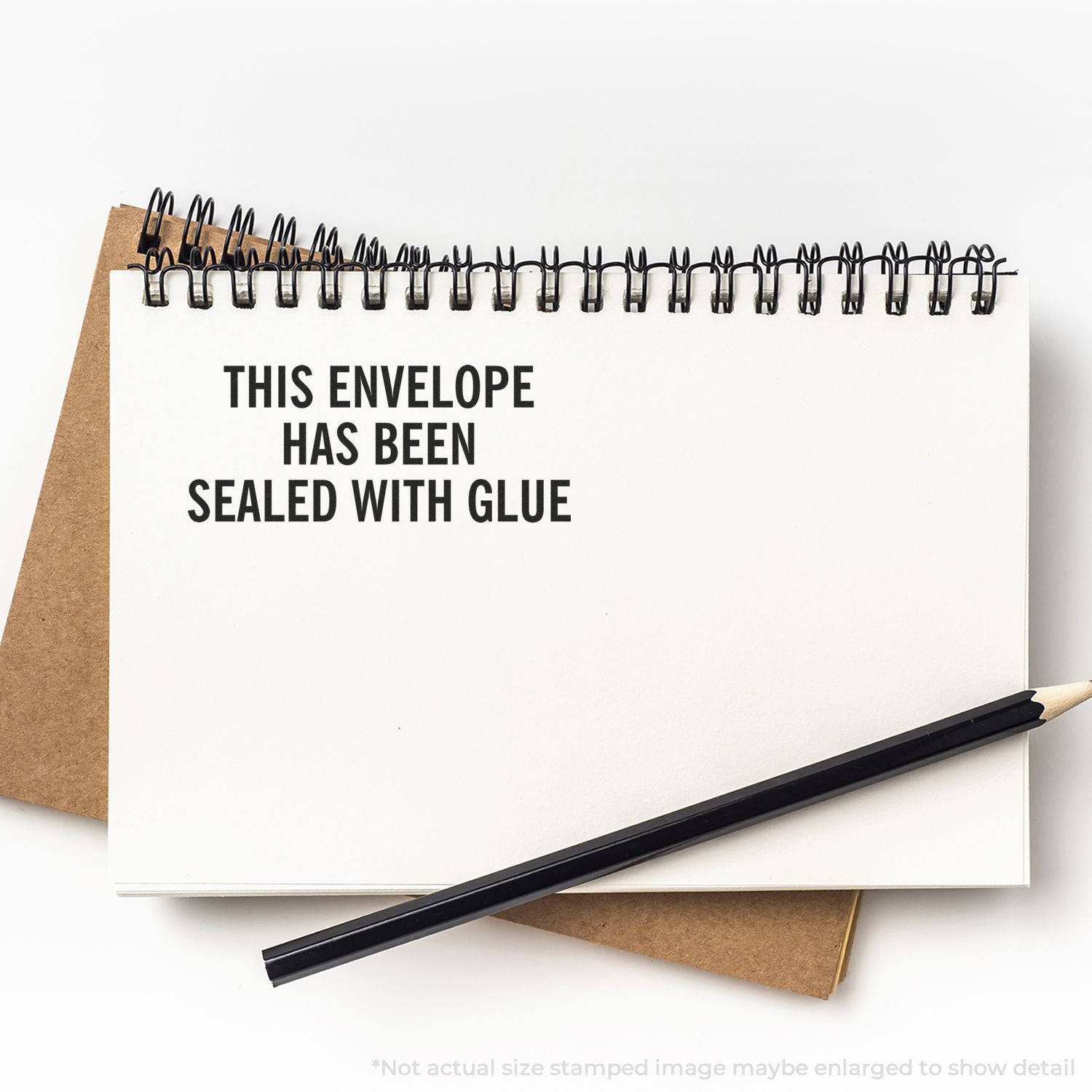 Spiral notebook with This envelope has been sealed with glue text, pencil, and brown envelope on white background.