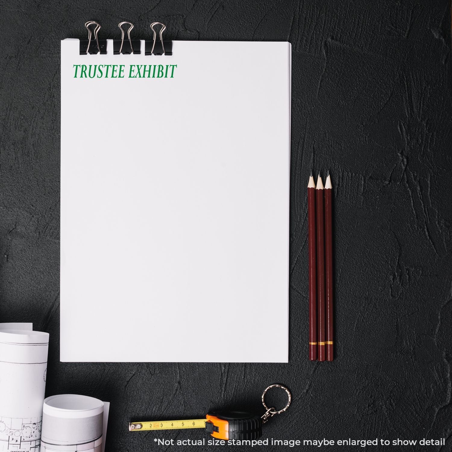 Blank trustee exhibit notepad with pencils, tape measure, and rolled blueprints on a black background.