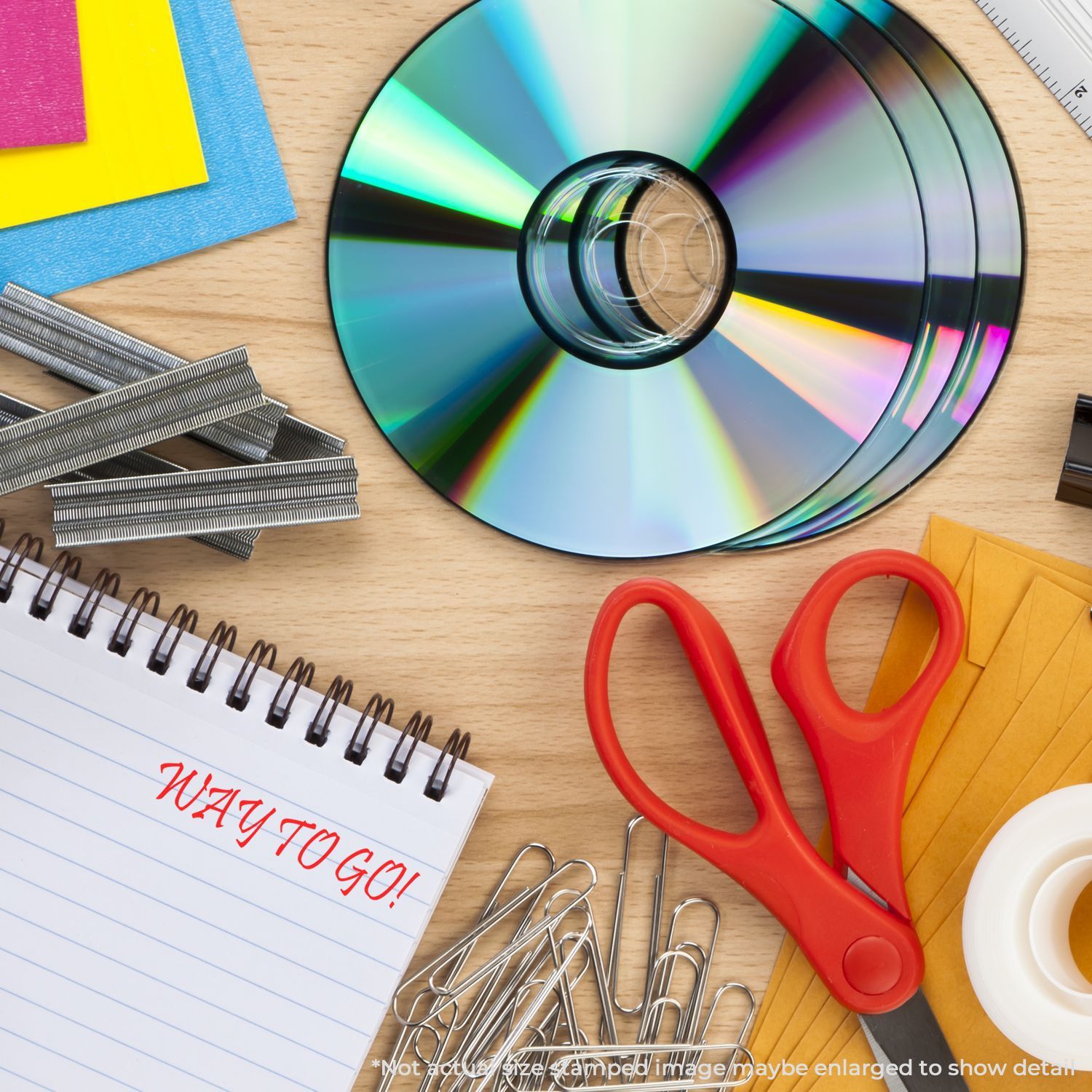 Rainbow CD/DVD data storage disc surrounded by office suppliesscissors, notebook, binder clipsshowing organization for tech projects.