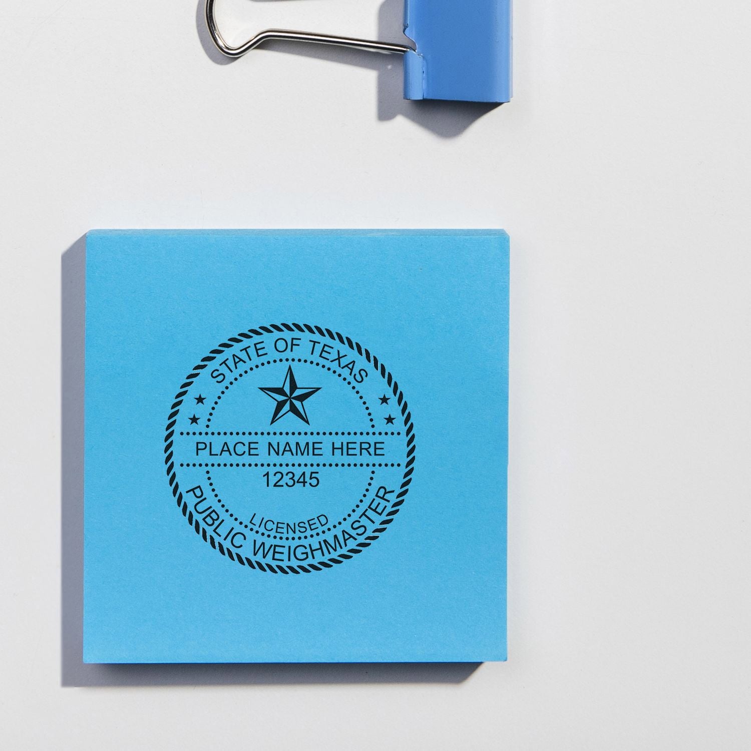 Blue Texas public weighmaster stamp template on a clipped note pad with blank place name and license number.