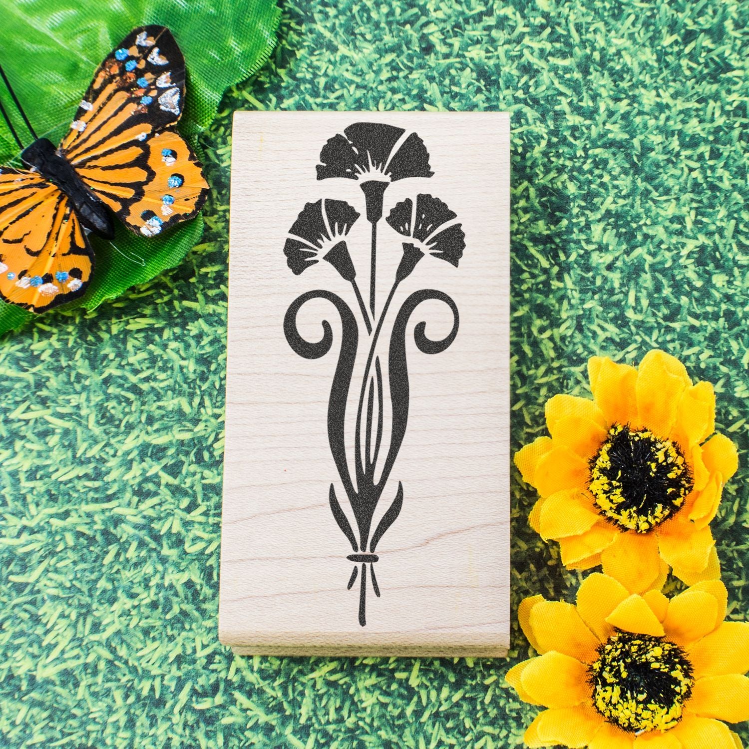 Butterfly and floral stencil on a wooden block with yellow flowers on a green grass background, decorative craft design.