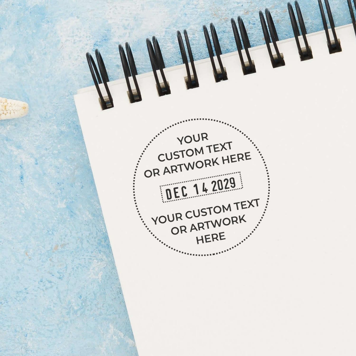 Spiral-bound notebook mockup with custom text and date stamp on a white cover against a blue textured background.