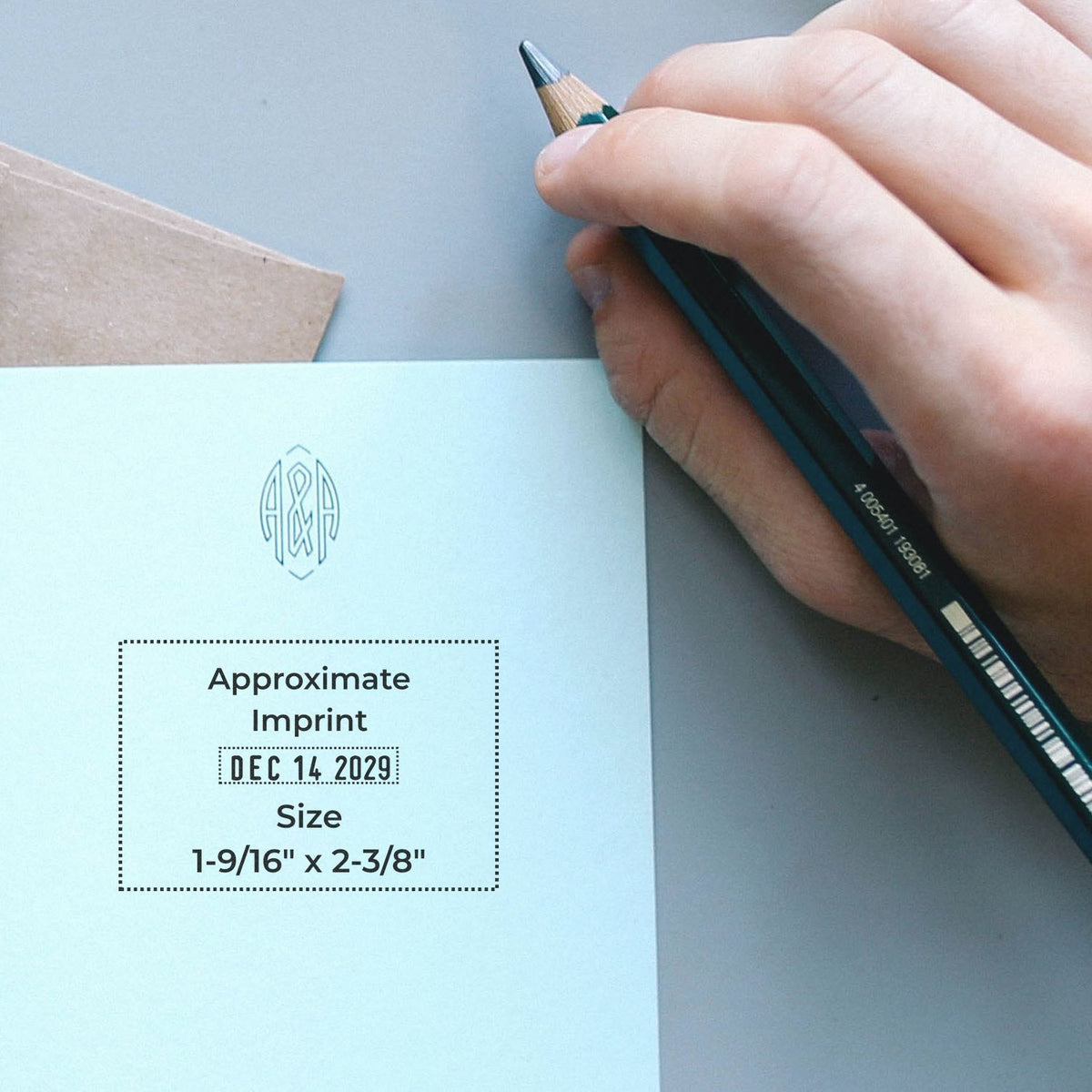 Hand holding pencil next to a custom monogram stamp imprint on an invitation, showing approximate imprint size and date.