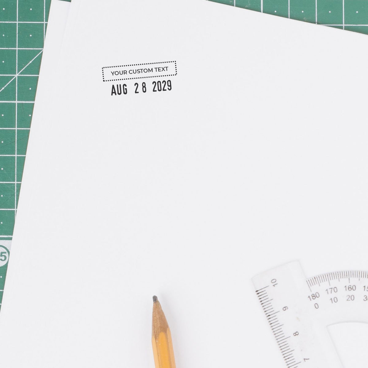 Blank custom text template on white paper with pencil, ruler, and cutting mat for stationery design and date stamping.