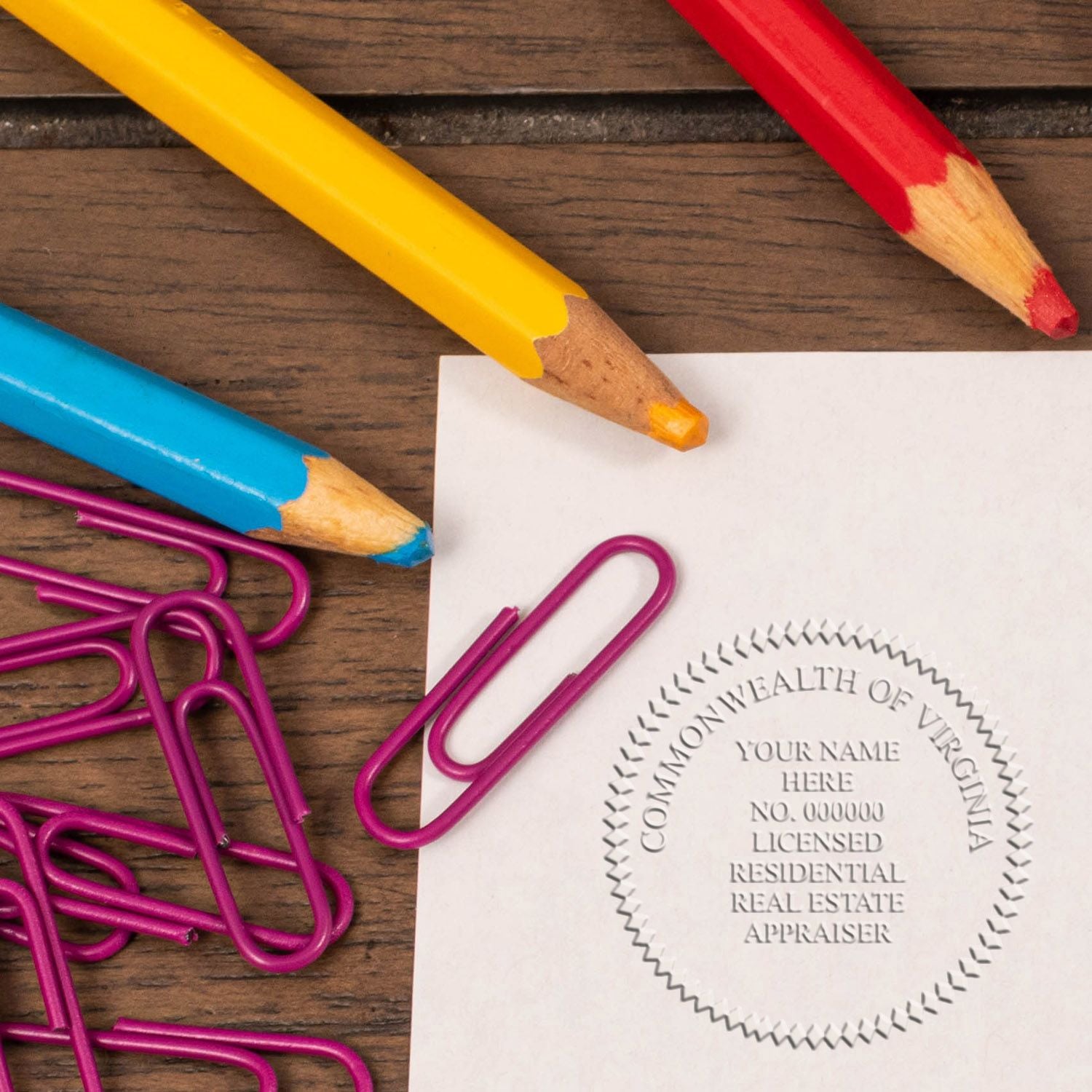 Colored pencils and paper clips beside a Commonwealth of Virginia licensed residential real estate appraiser seal on white paper.