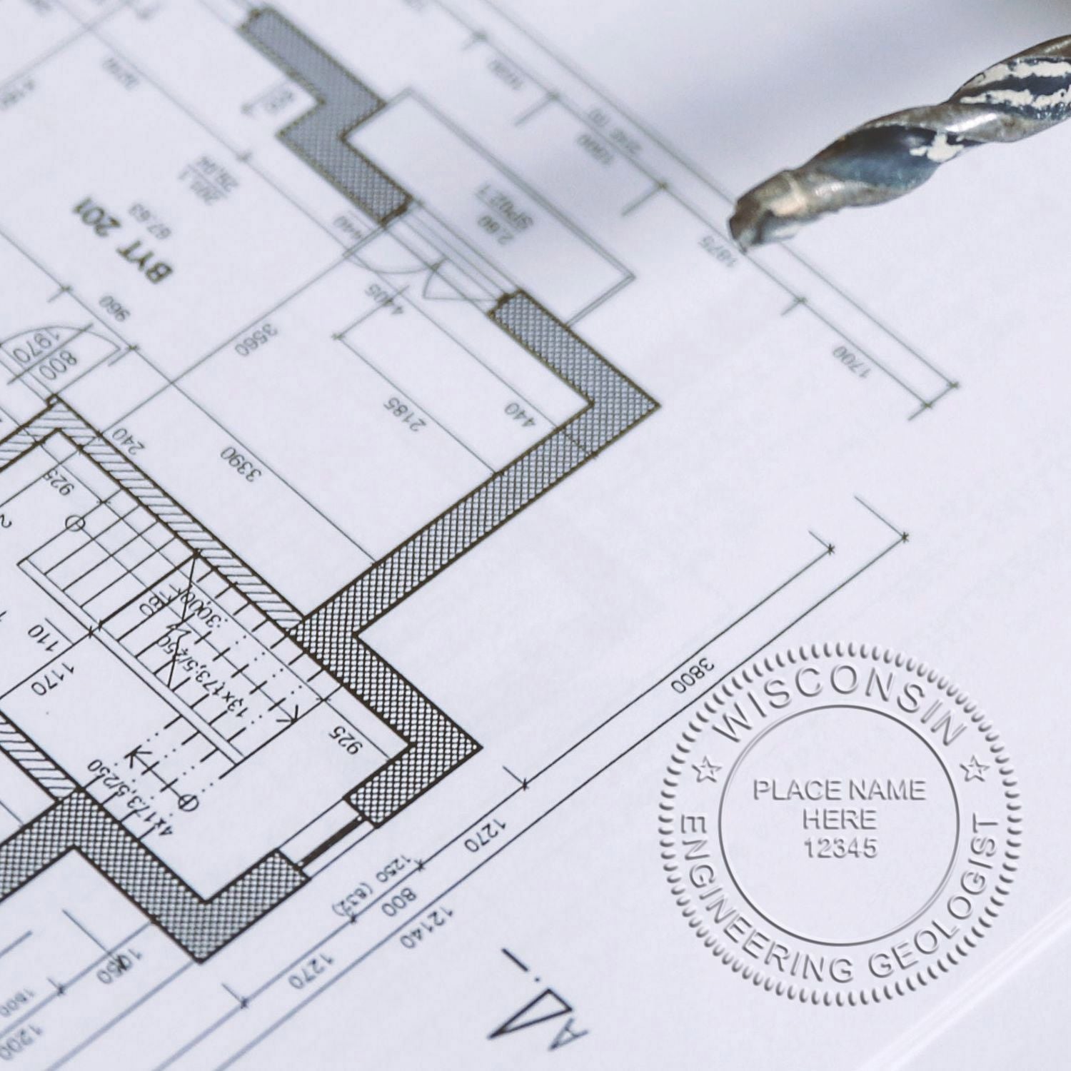 Close-up of an architectural blueprint with a drill bit and Wisconsin engineering geologist seal.
