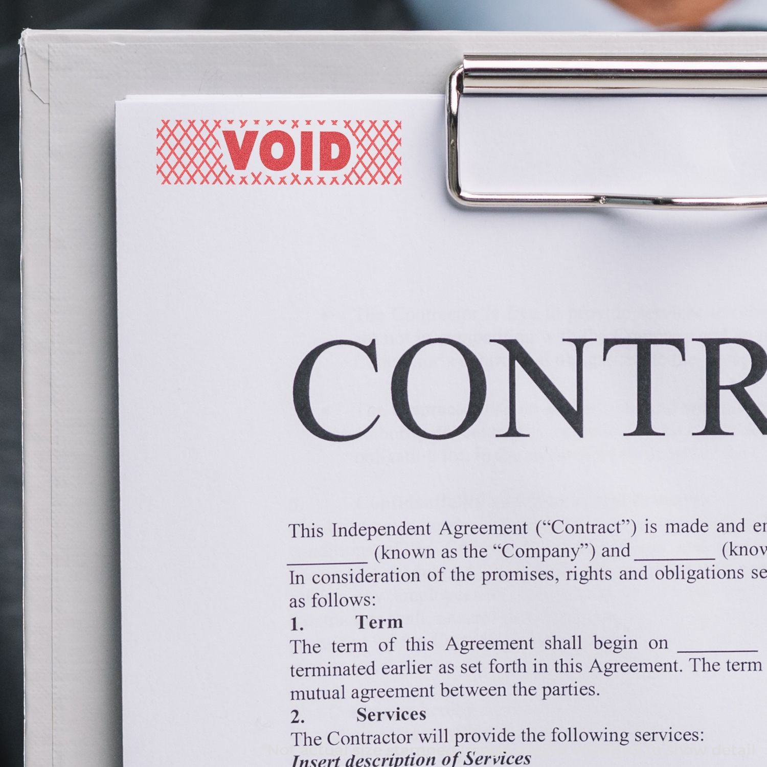 Red VOID stamp on a contract document clipped to a clipboard, marking paperwork as canceled or invalid in an office setting.