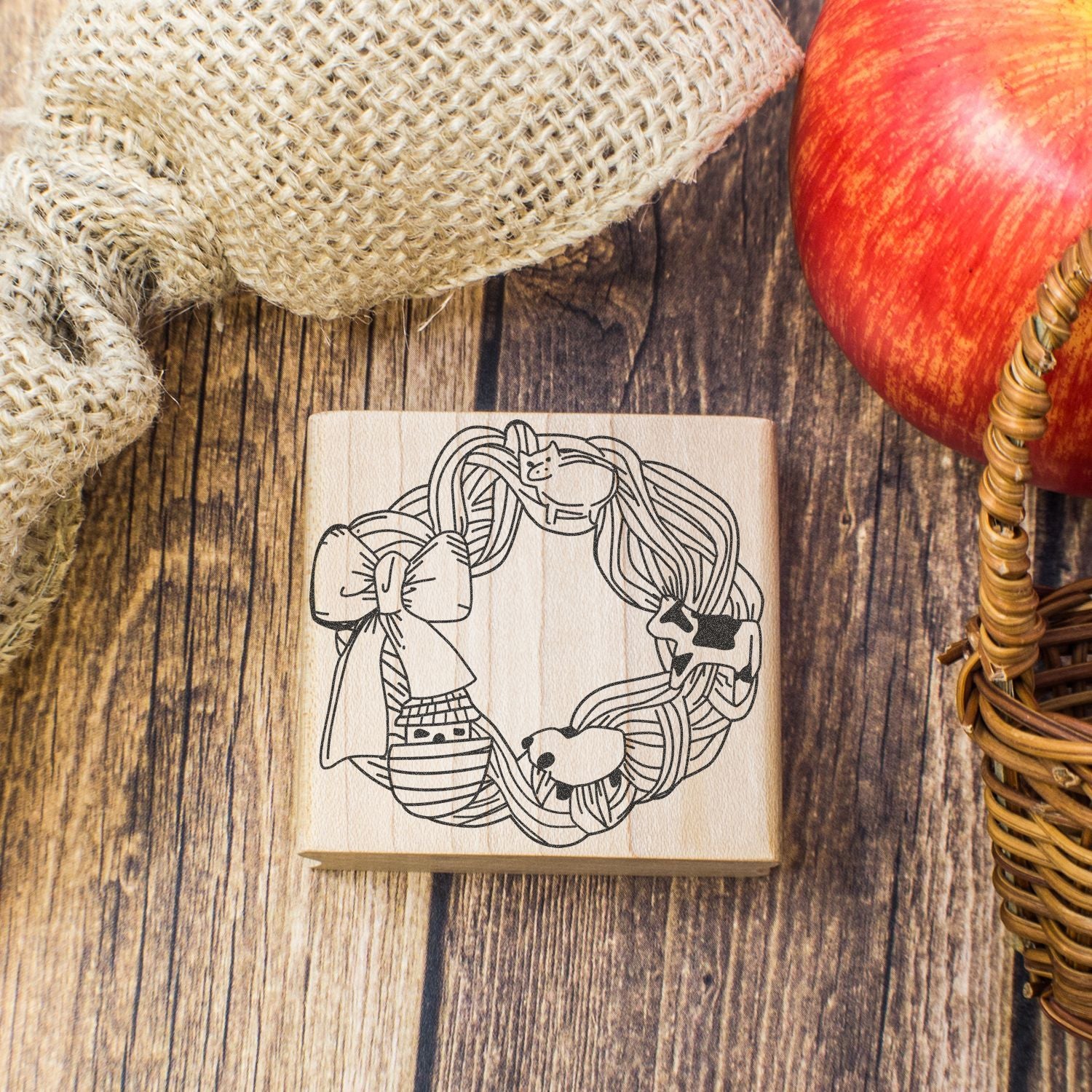 Autumn wooden stamp with fall wreath and pumpkins, styled with burlap, red apple, and rustic farmhouse decor on a wood background.