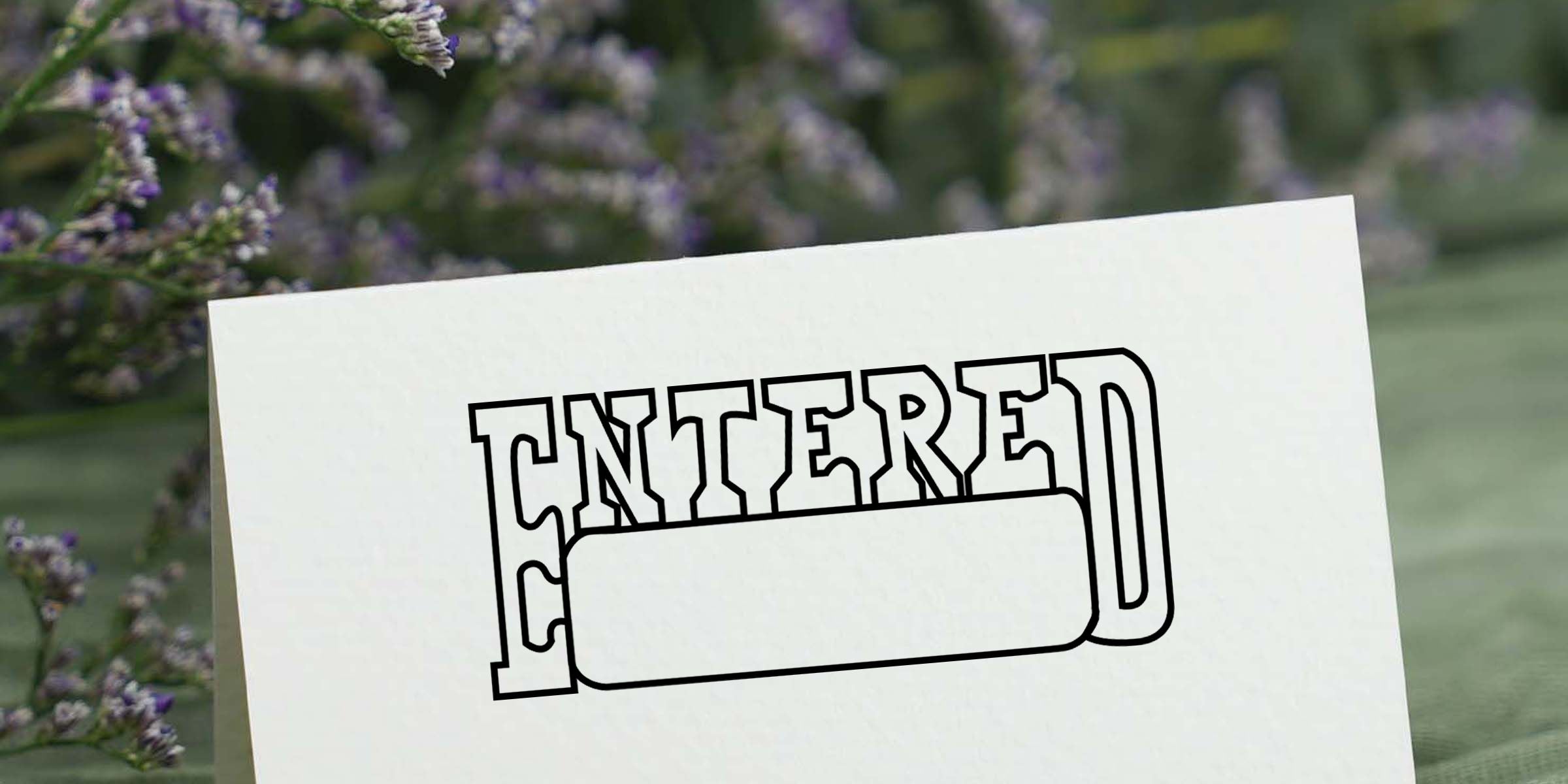 White card with bold outlined “ENTERED” text displayed against a blurred lavender field background outdoors