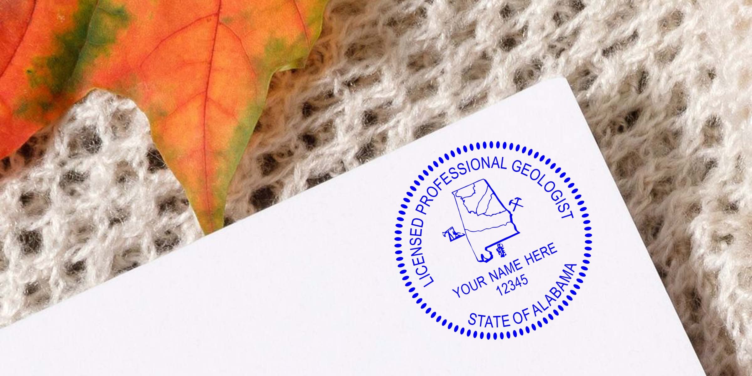 Licensed Alabama Geologist Stamp on white paper with autumn leaf and knitted fabric background, plus tips for purchasing the Alabama Geologist Stamp.