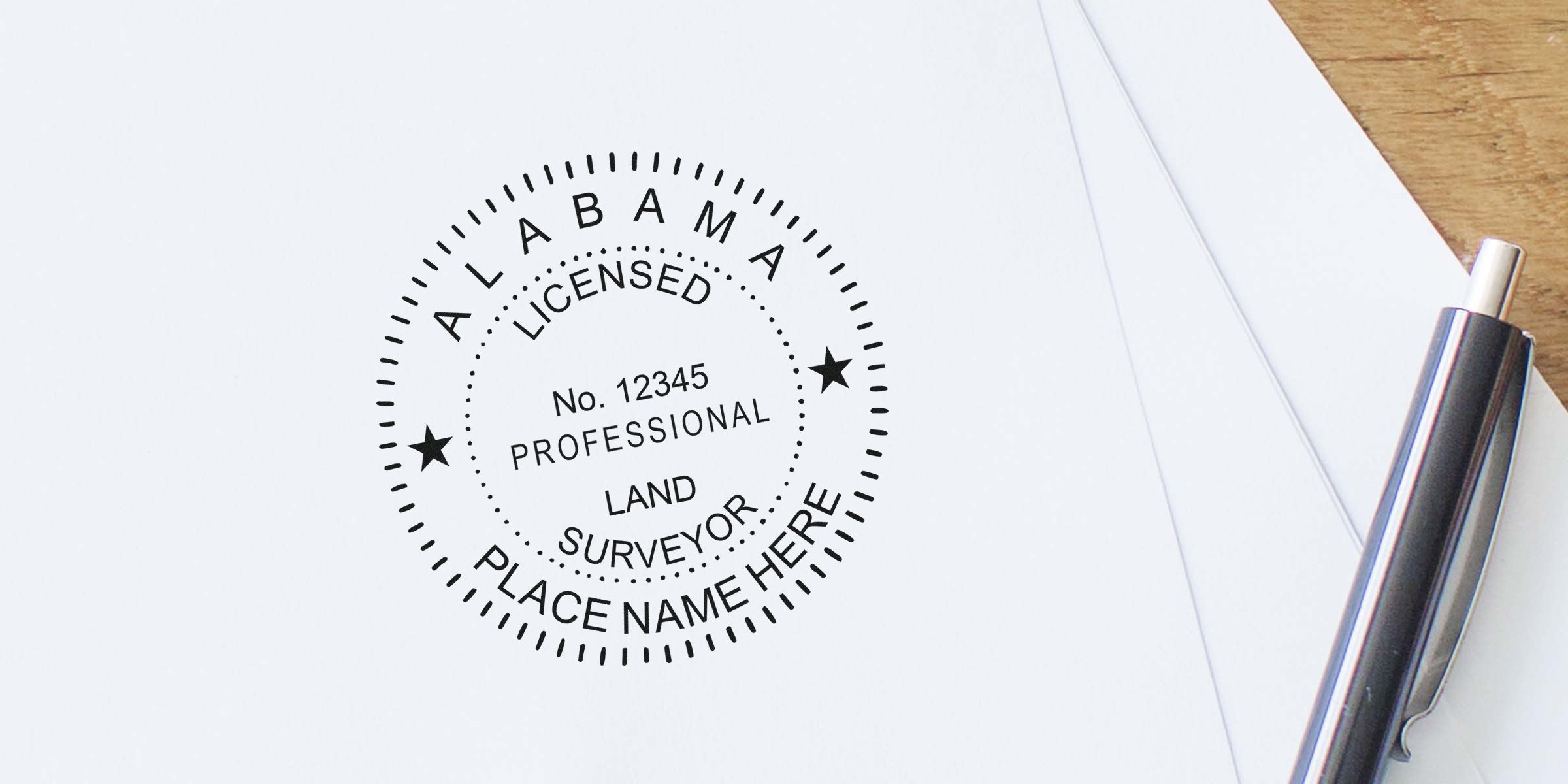 Custom Alabama land surveyor seal and stamp on white paper with a pen.