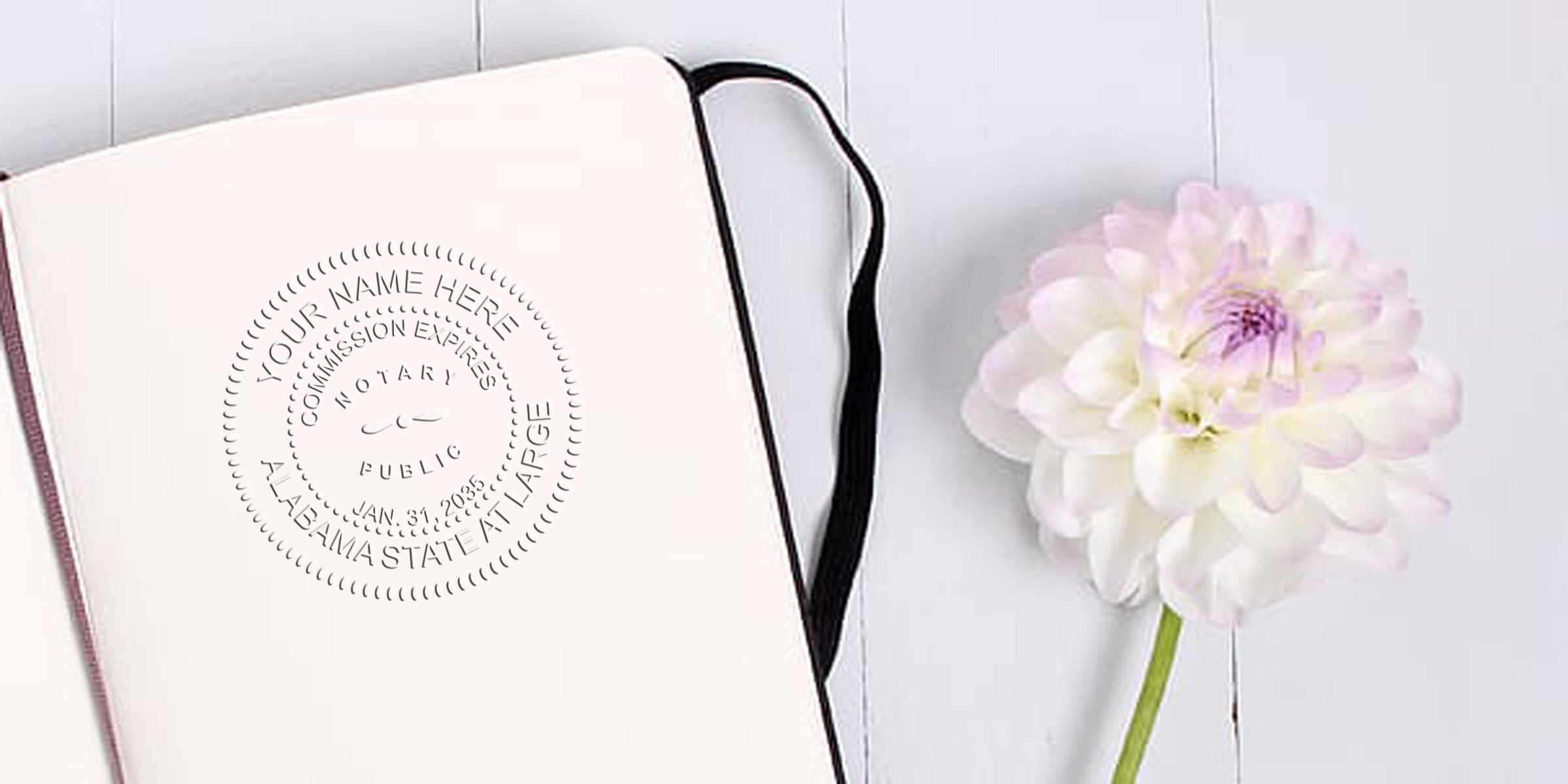 Notary stamp on open notebook with white flower on wood background, showing Alabama state commission expiration date, highlighting essential Alabama notary supplies and tools.