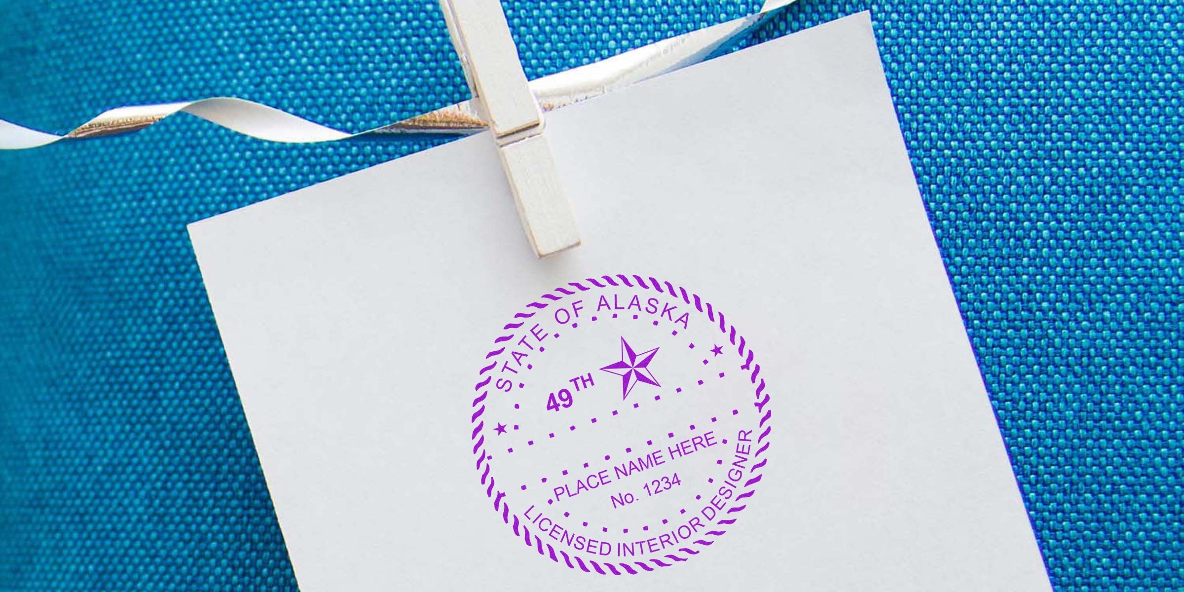 Alaska interior designer stamp on white paper clipped with clothespin against blue fabric, symbolizing interior design licensing in Alaska.