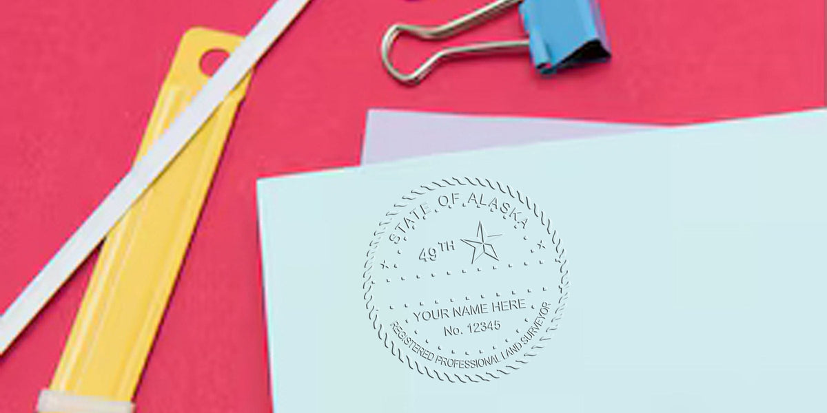 Embossed Alaska professional land surveyor seal on blue paper with office supplies on red background, highlighting Alaska land surveyor fees and stamp prices.